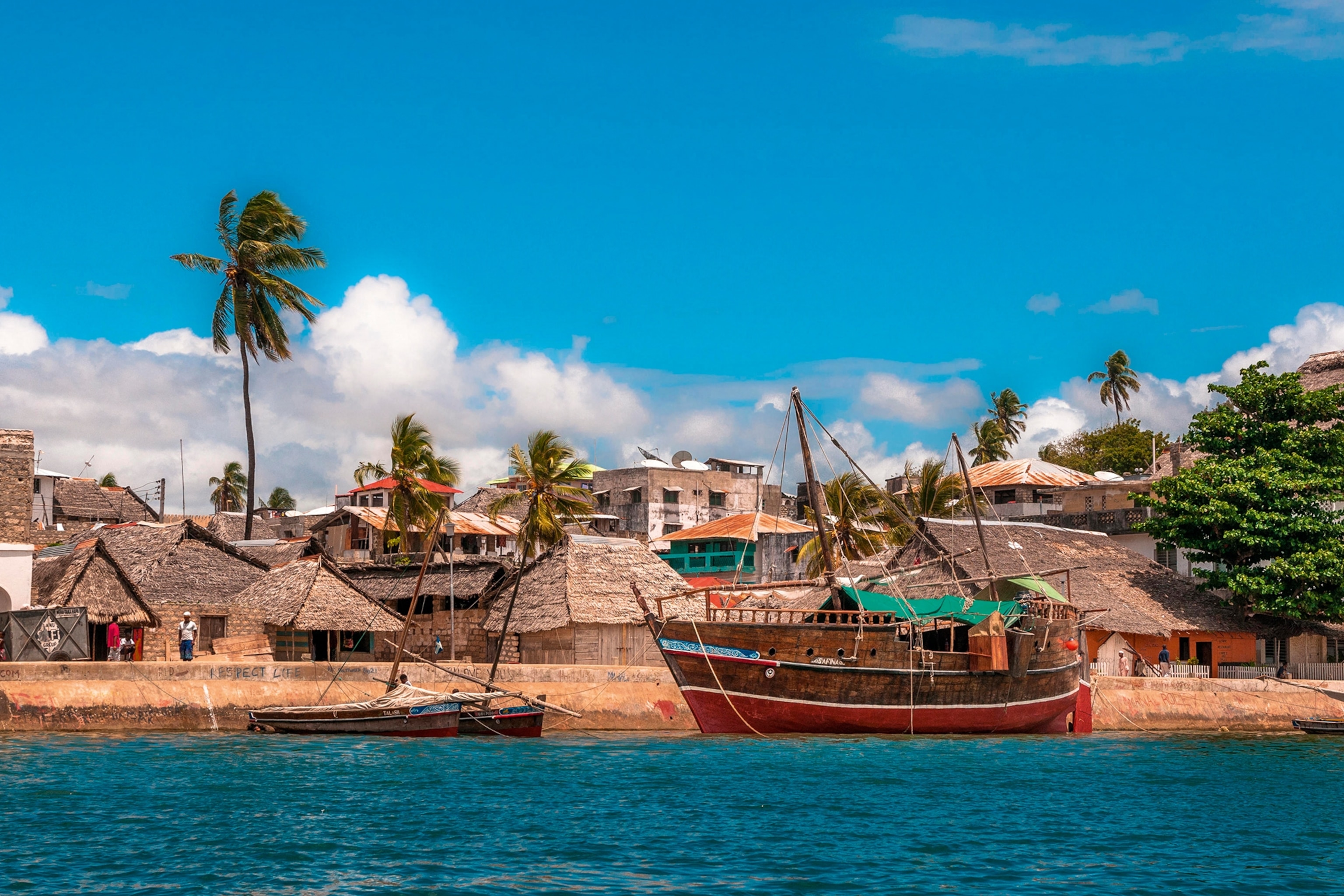 A small waterfront village in Kenya with a couple of wooden boats anchored in front.