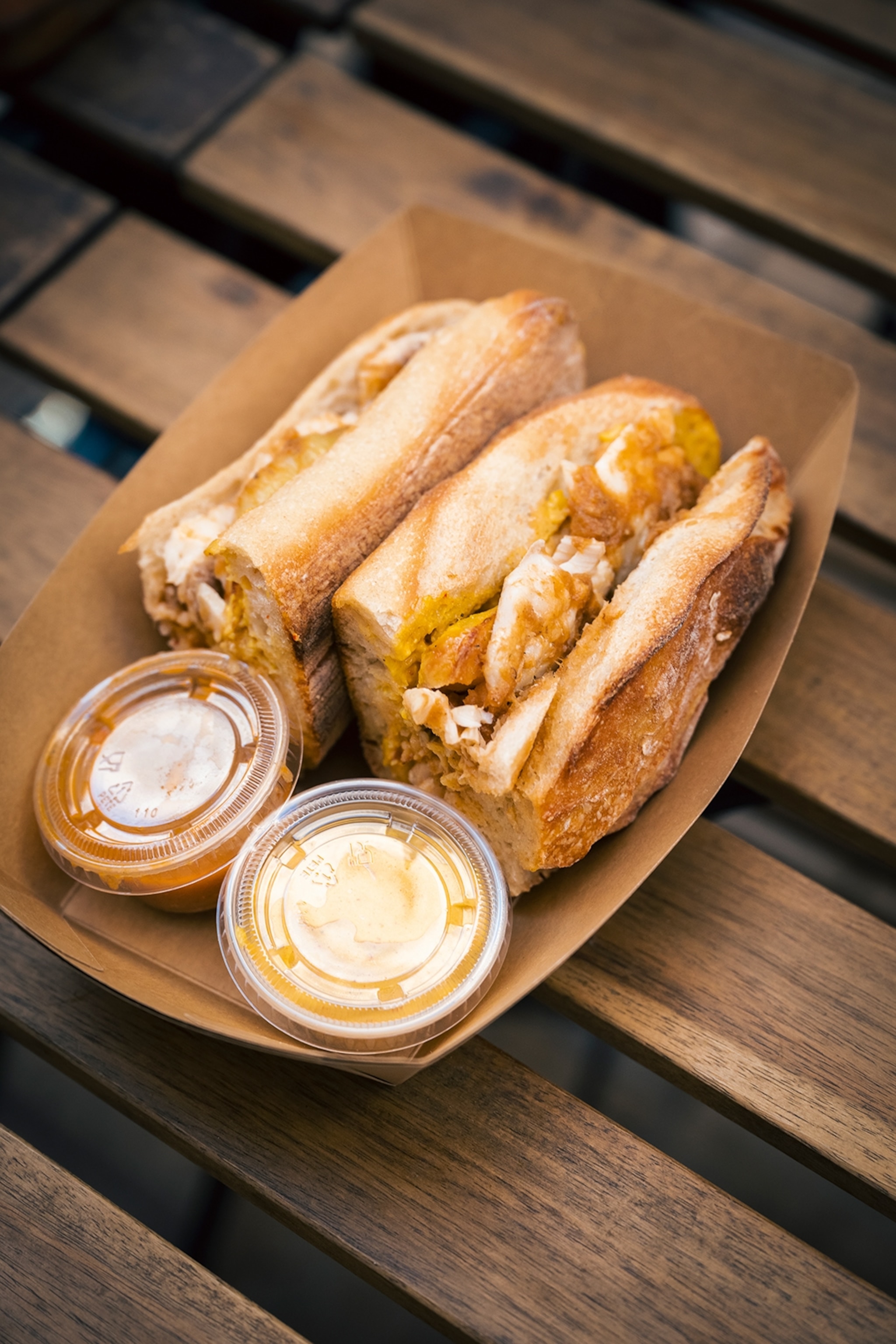 A sandwich filled with fish and served with tiny tubs of dips and soup.