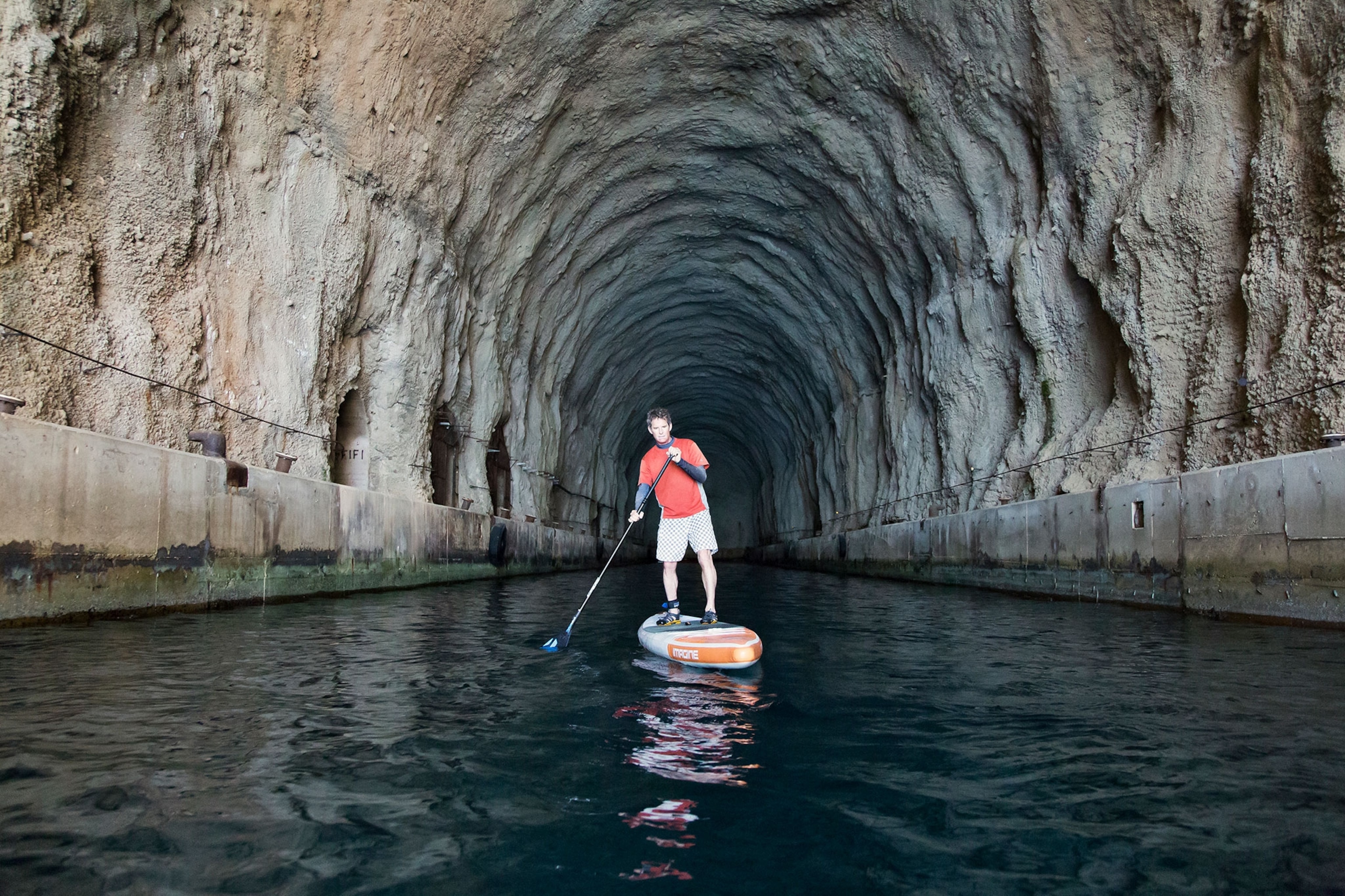 a stand-up paddle boarder paddling through a Cold War submarine cave in Croatia