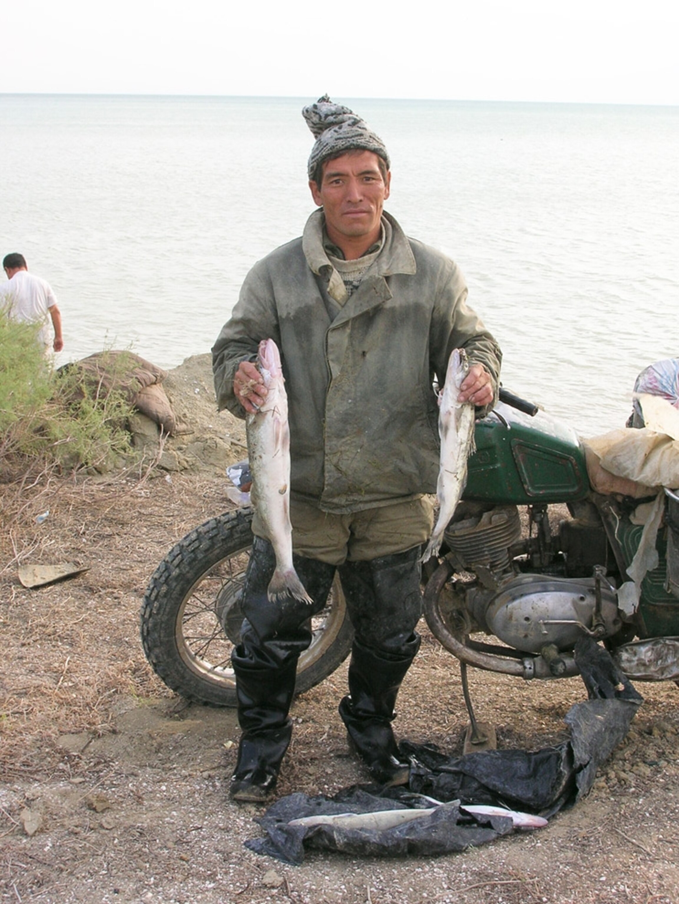 Man holding two fish in front of a motorcycle