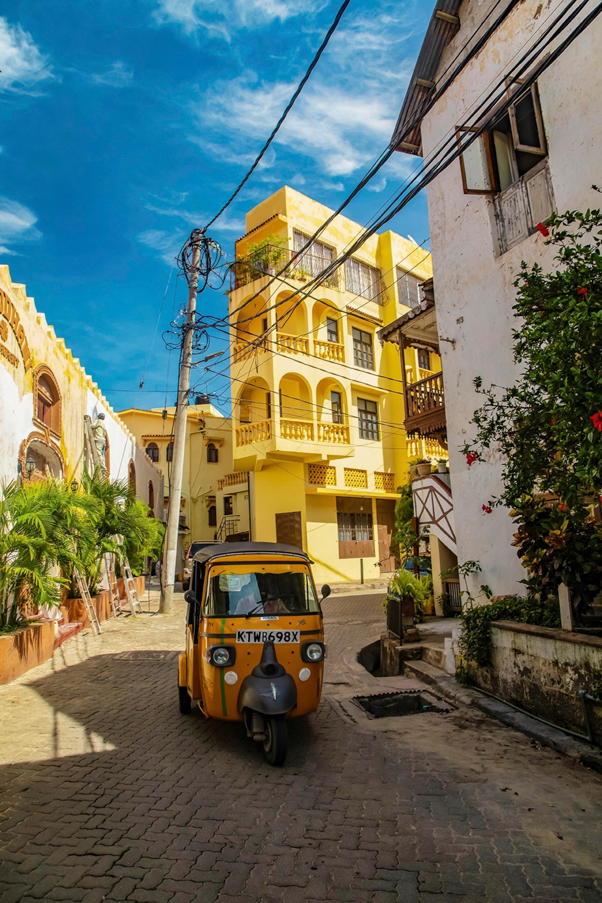 A tuk-tuk navigating through a quiet side street surrounded by European-style architecture.