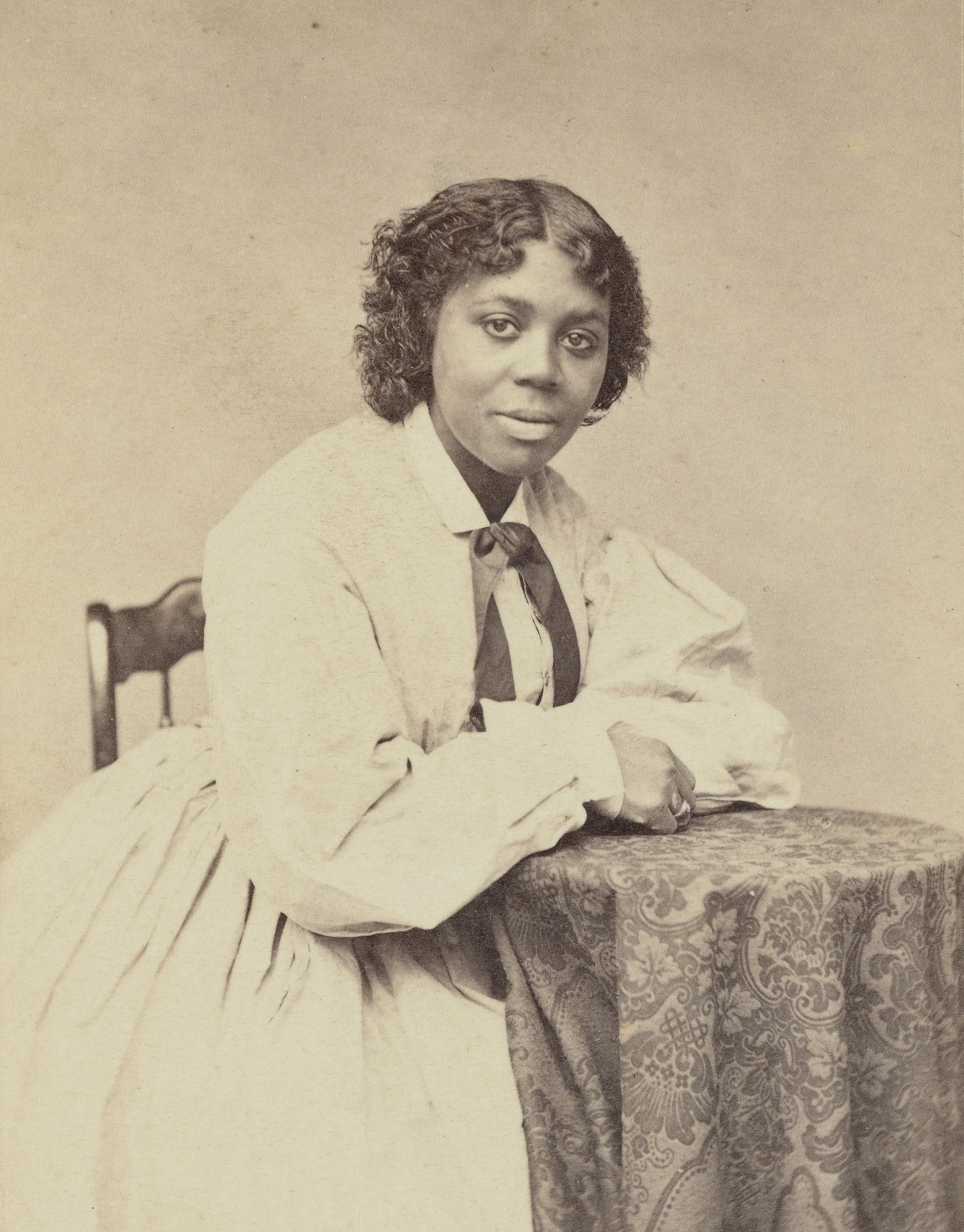 A Black woman in a white dress sits for a portrait, sepia