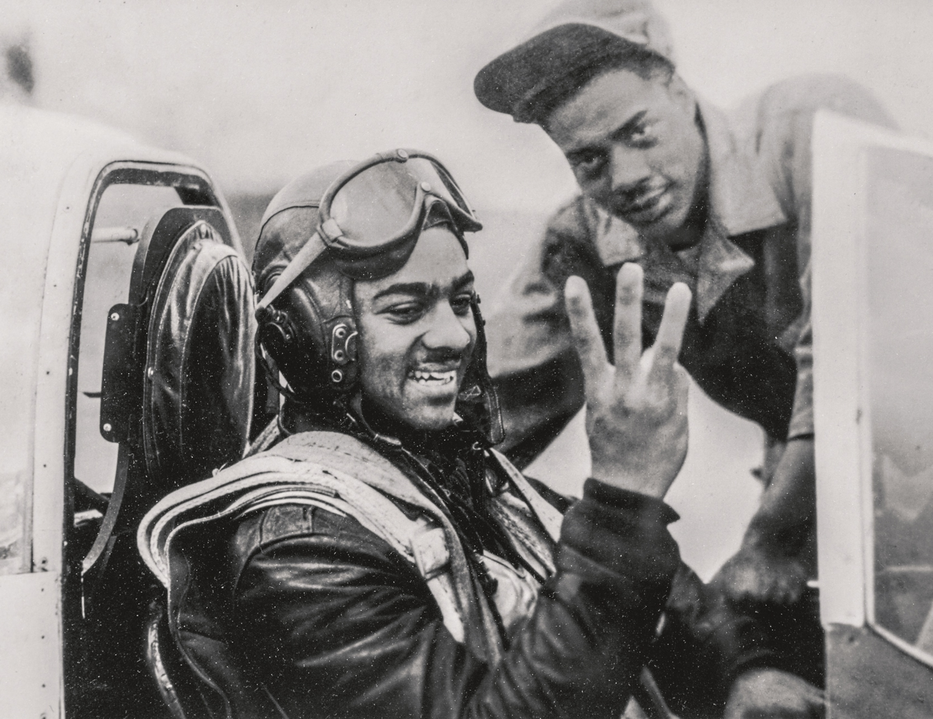 a two men, one in an fighter jet holding up three fingers