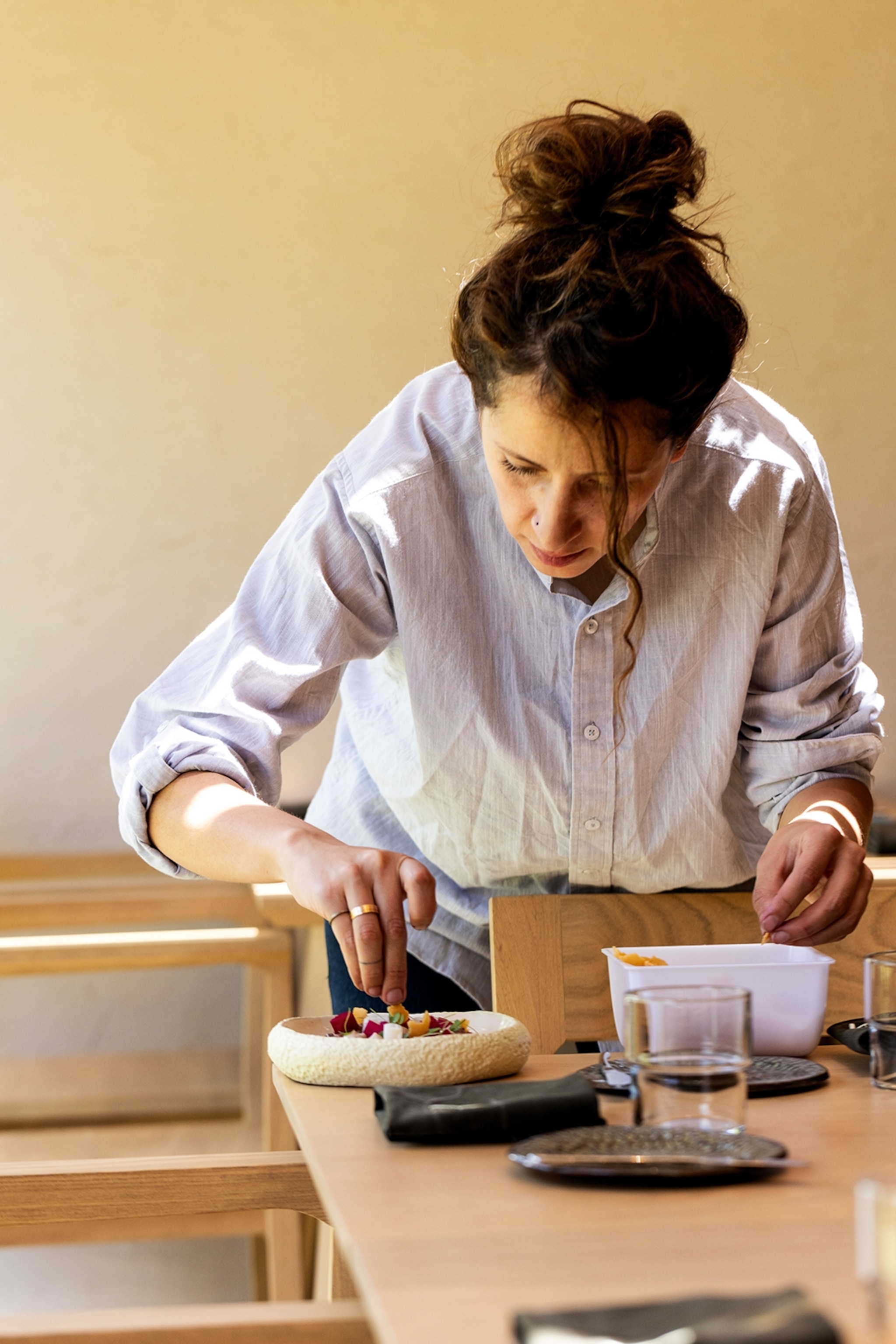 A young, female chef adding final touches to a small plate in a sleek outdoor retstaurant setting.
