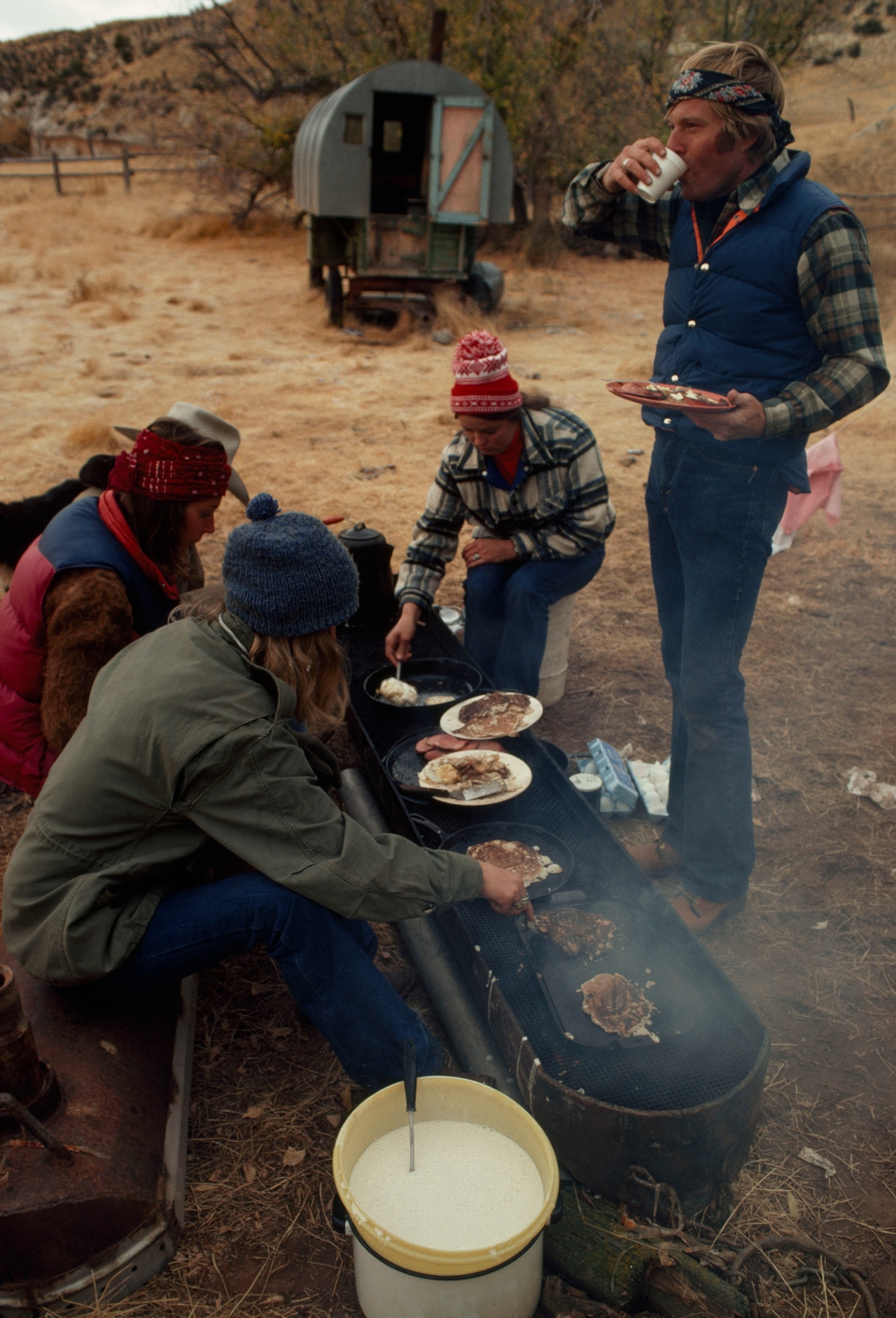 A group of people surround an elongated grill outside