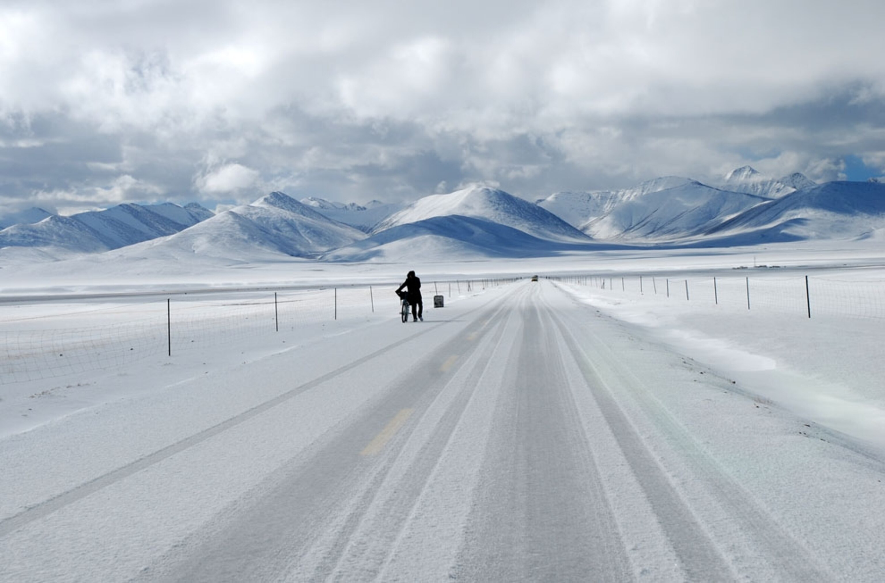 Person walking their bike along a snow-covered road in Tibet