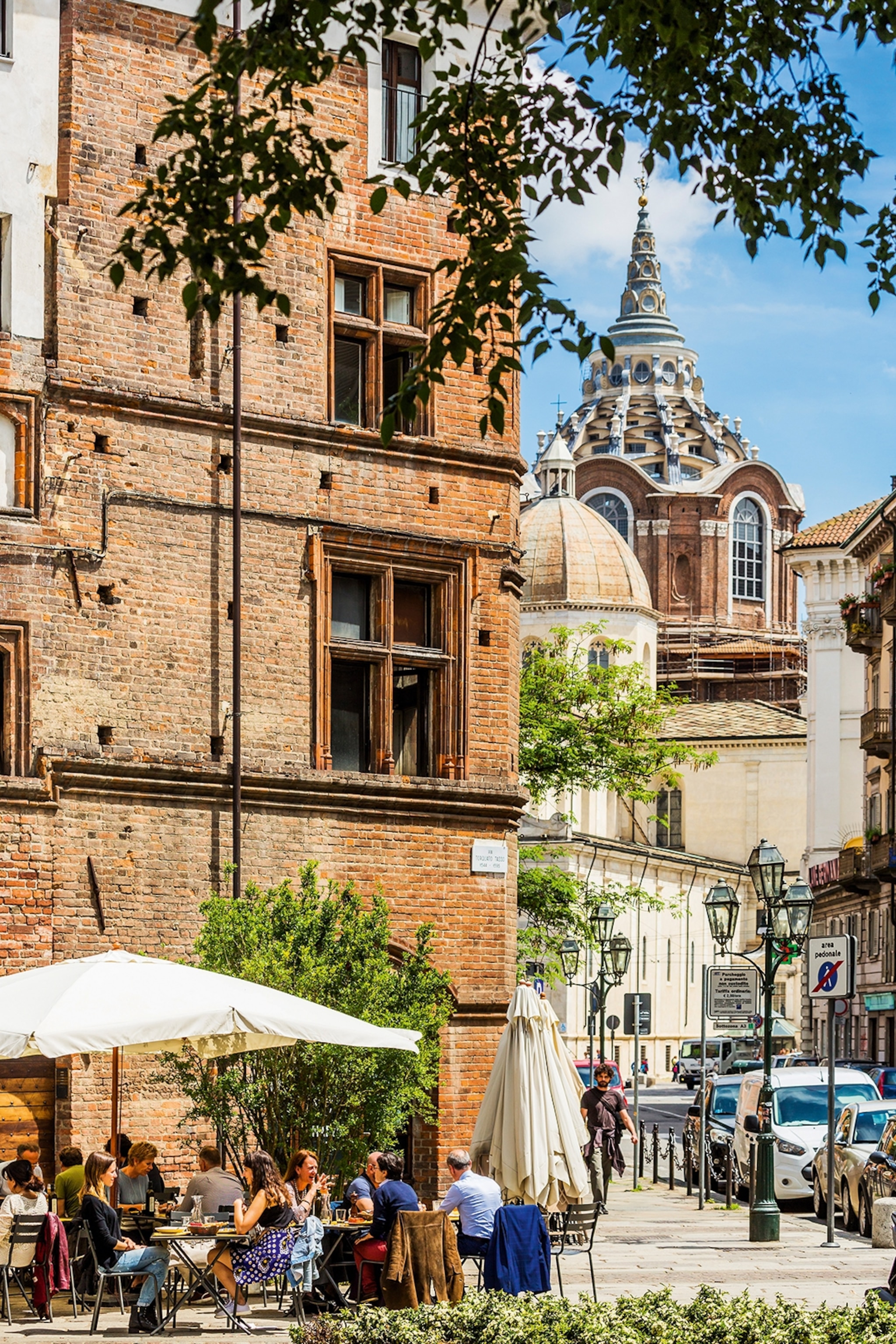 A busy city scene in summer with people sitting under a canopy and a chapel tower in the background.