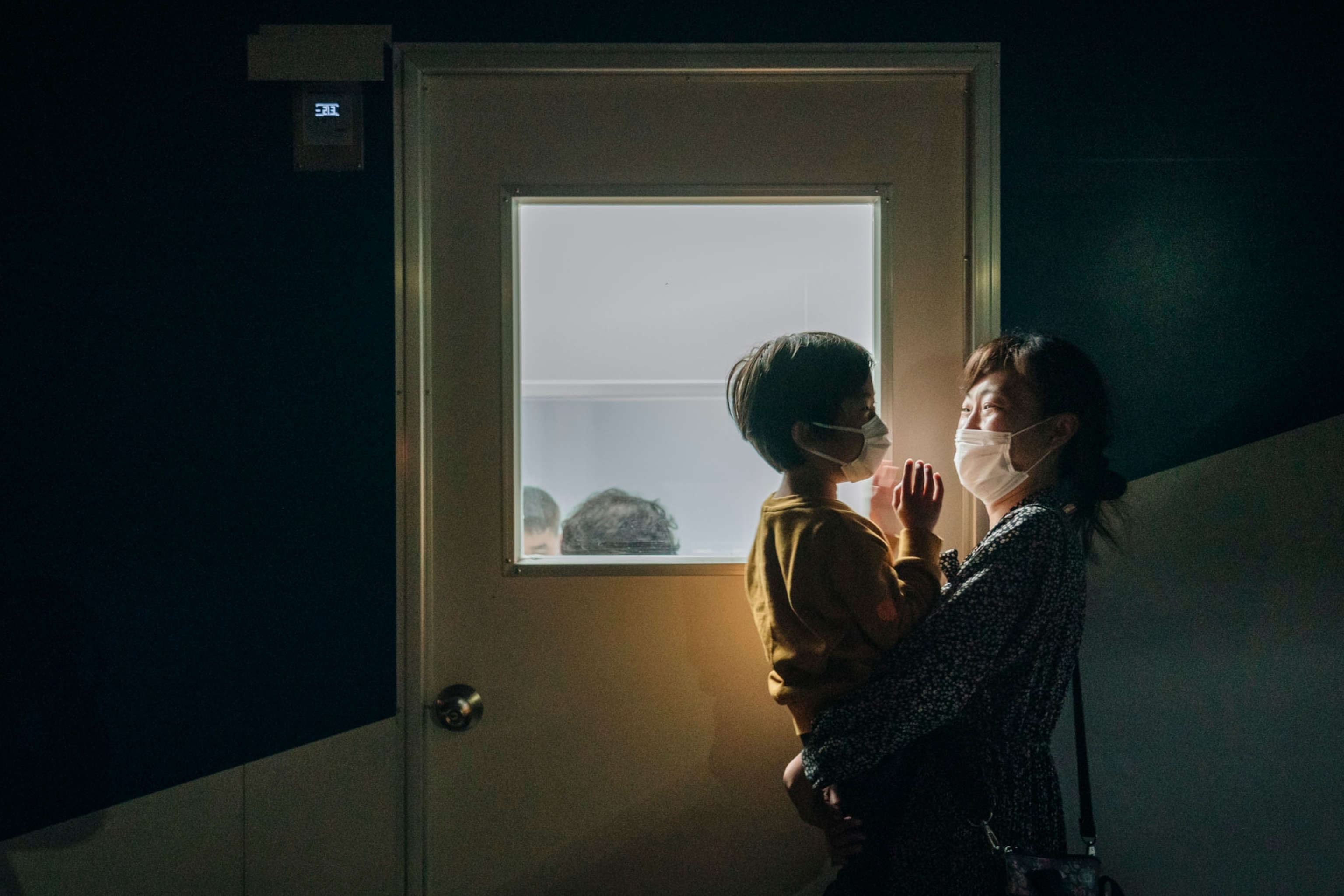 a woman holding a child next to a window with a door, overlooking the water
