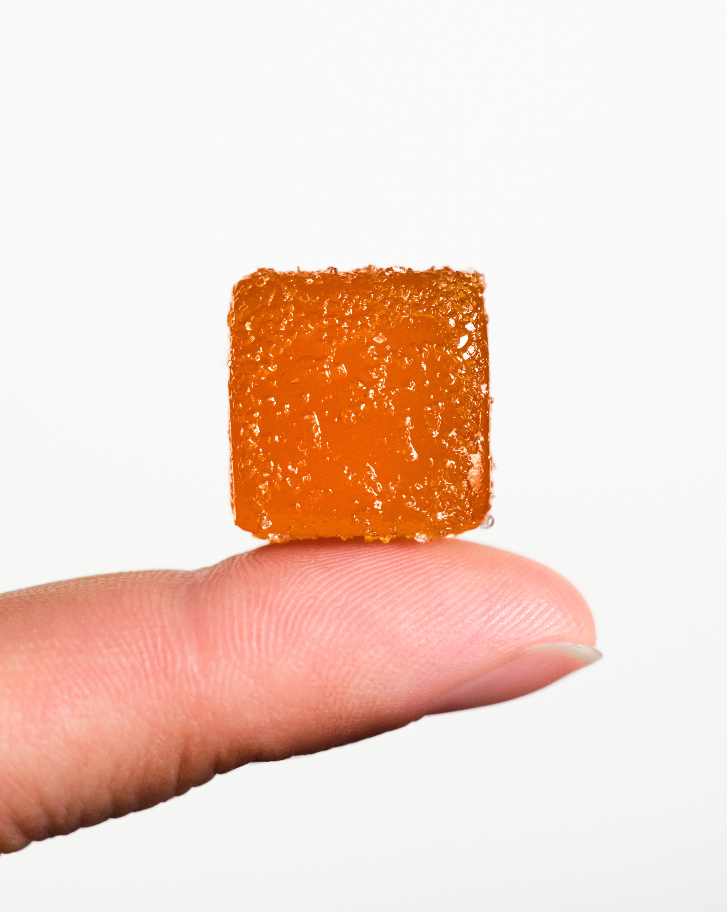 Orange gummy displayed on human the tip of human finger.