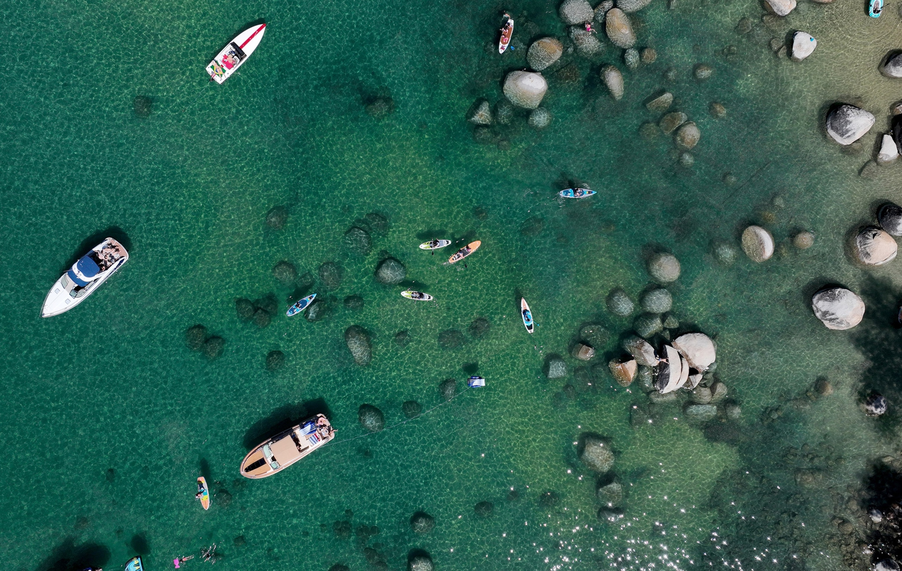 An aerial shot looking down at green waters dotted with rocks, boulders, kayaks, and boats