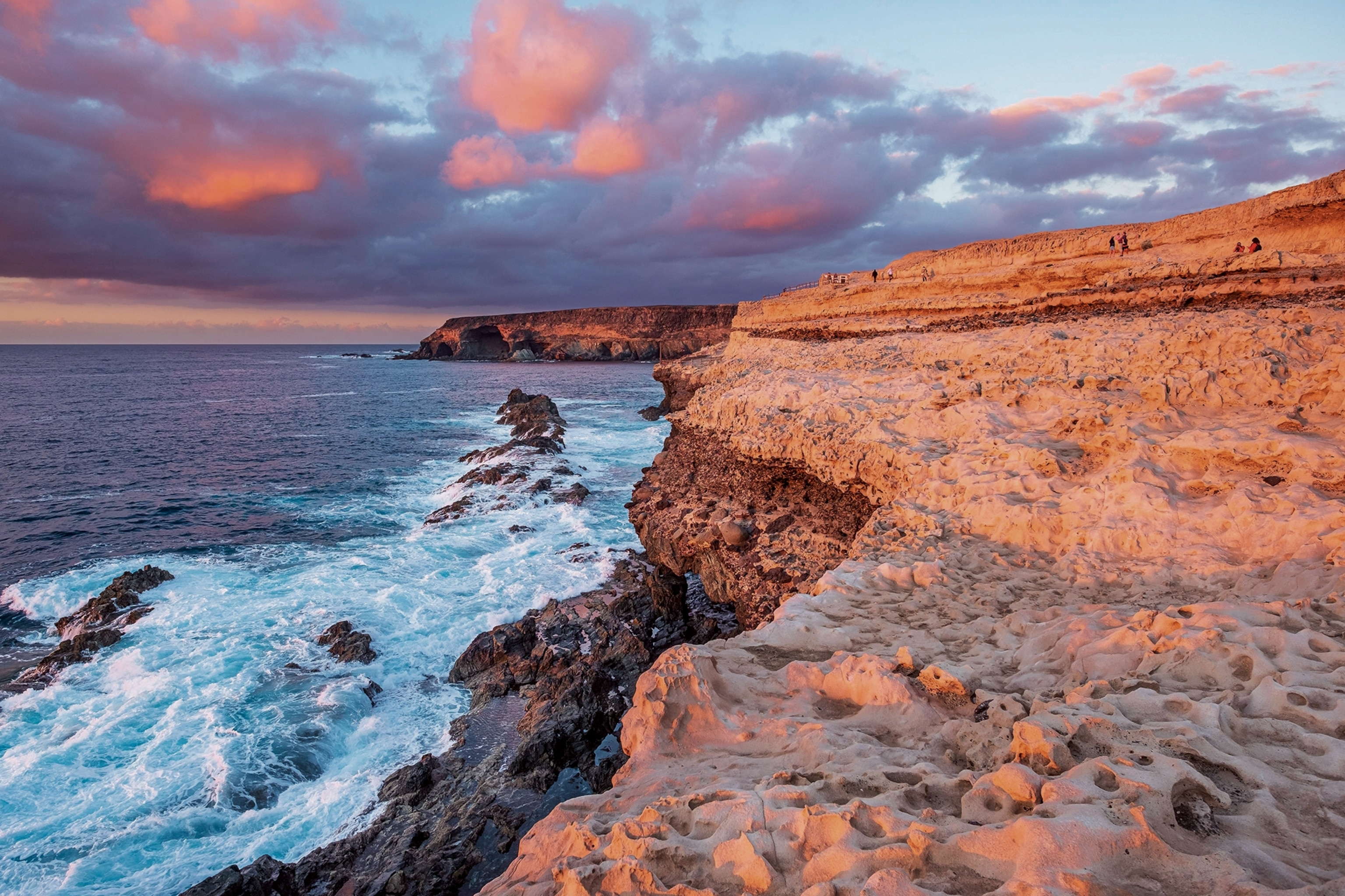 A seaside cliff in a moody sunset lighting with waves crashing against rocks on the shores.
