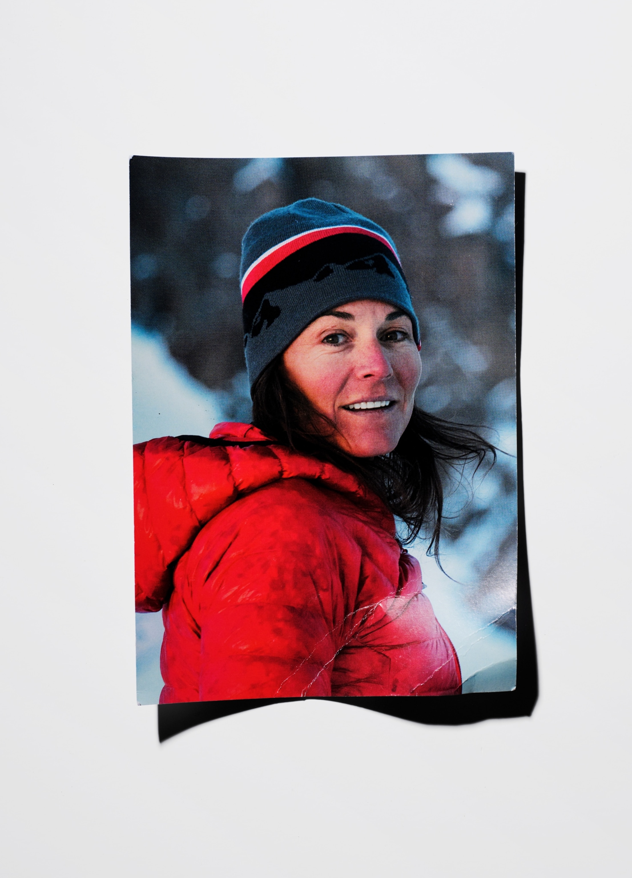 A photo of Hilaree Nelson wearing a red puffer jacket and a striped beanie. The photo lies on a white background