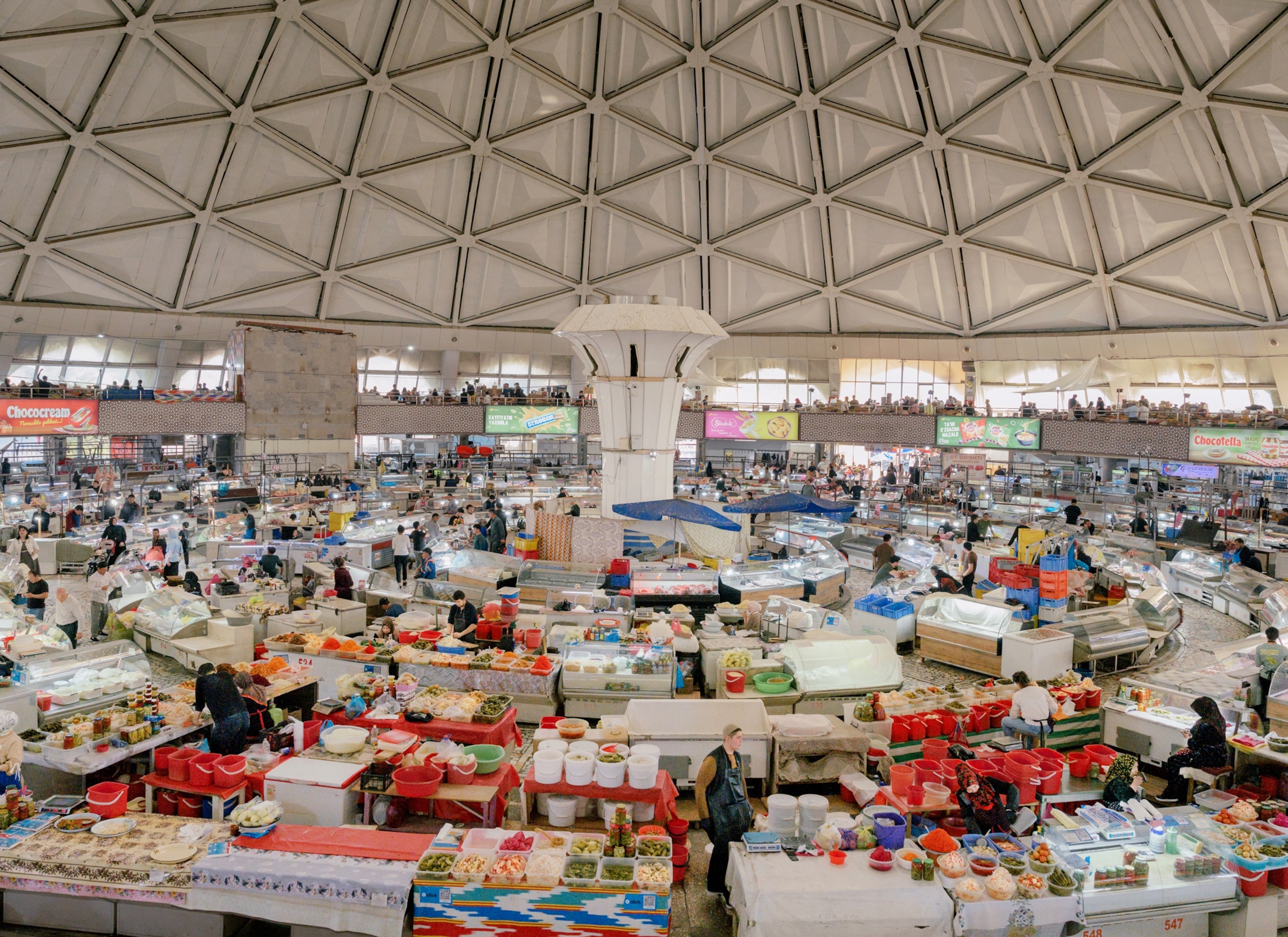 A large indoor market in a circular room with numerous food stands packed tightly together