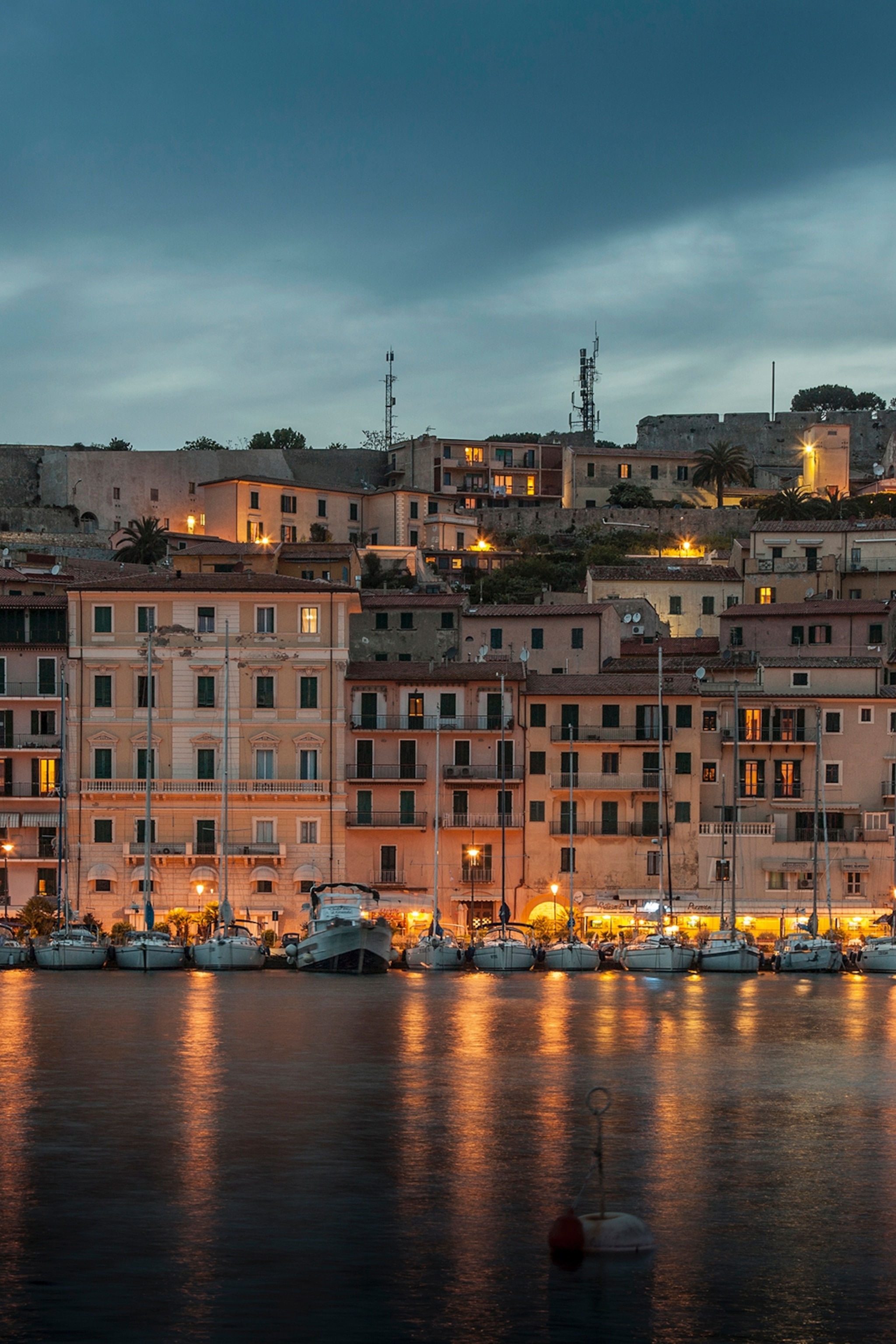 The promenade of an Italian sea-side town at late dusk with romantic lights illuminating the pink houses.