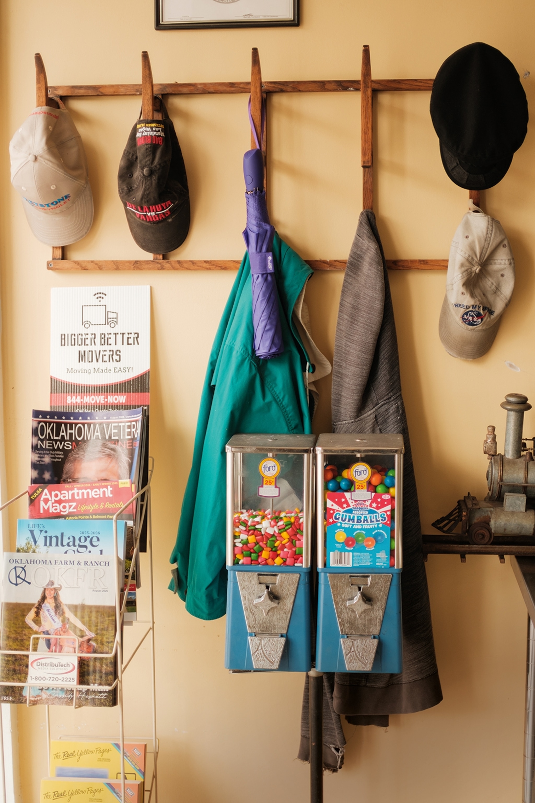 A coat hanger with hats hung in a row above, next to a magazine stand and retro gumball vending machines.