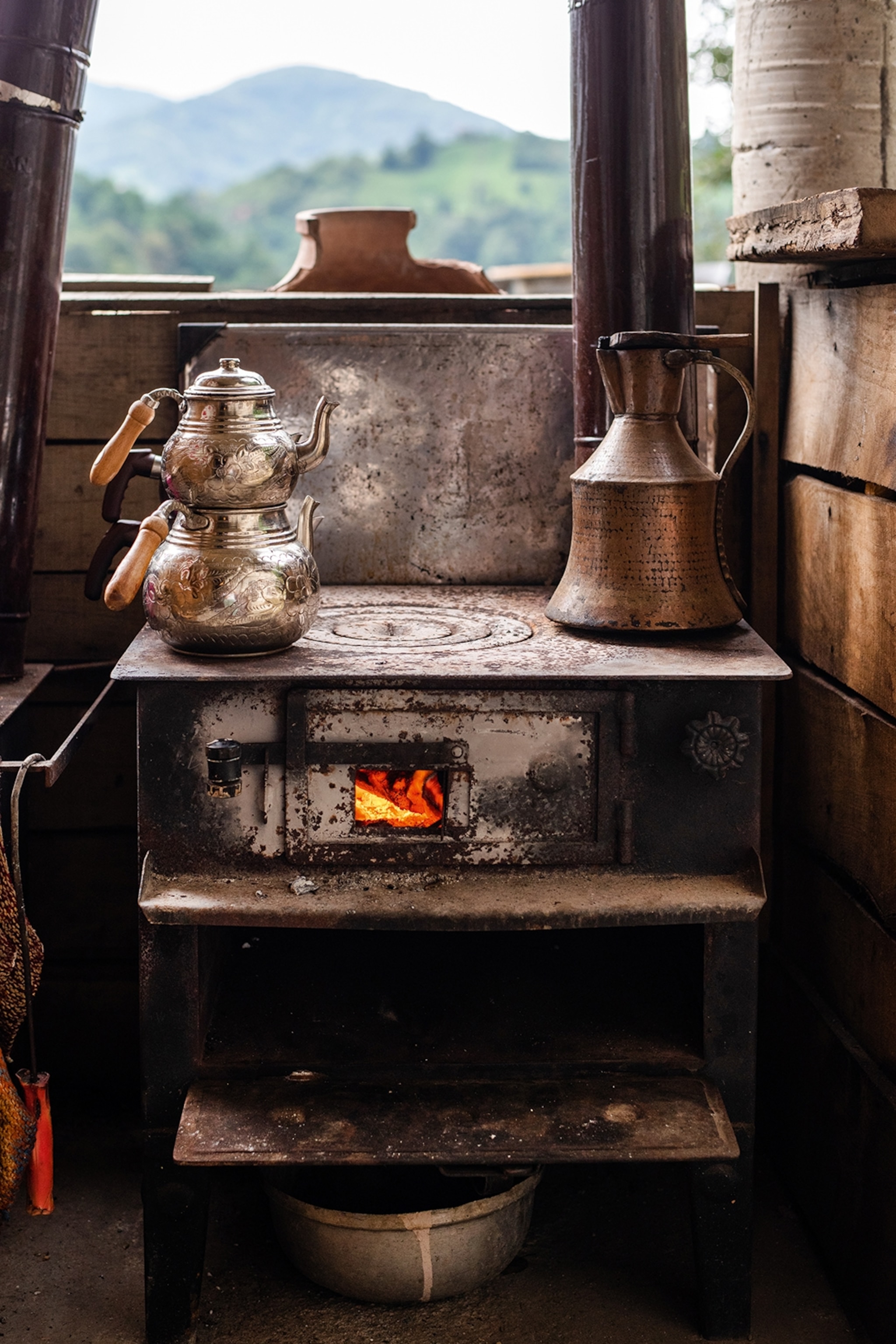An old-school aga oven with a double tinned tea pot sitting on top and view of the mountains stretching behind it.