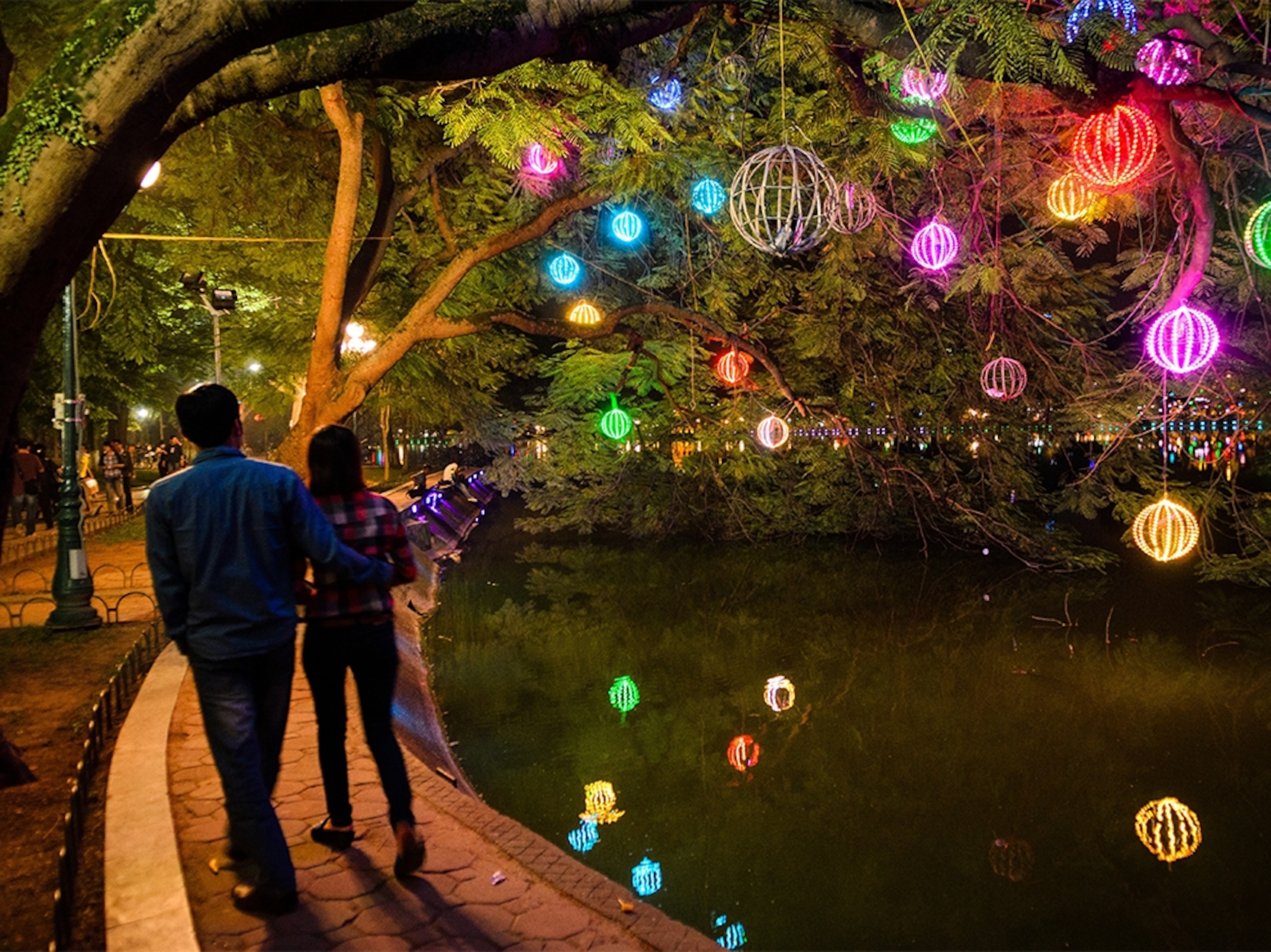 a couple walking past Hoan Kiem Lake in Hanoi, Vietnam with colorful lanterns above
