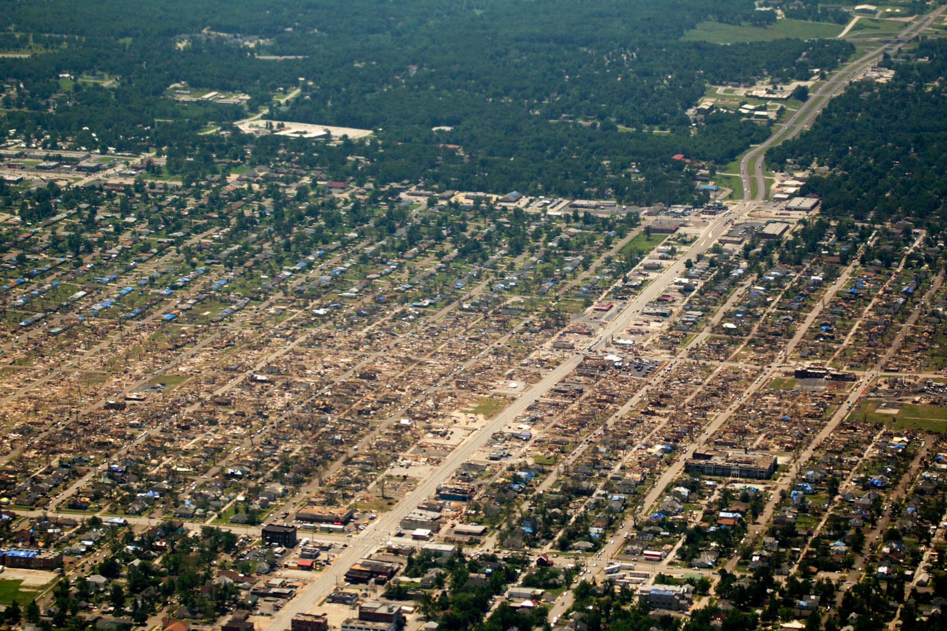 An aerial view of a neighborhood partially destroyed by a tornado. A line of destroyed houses is visible between rows of still standing houses.