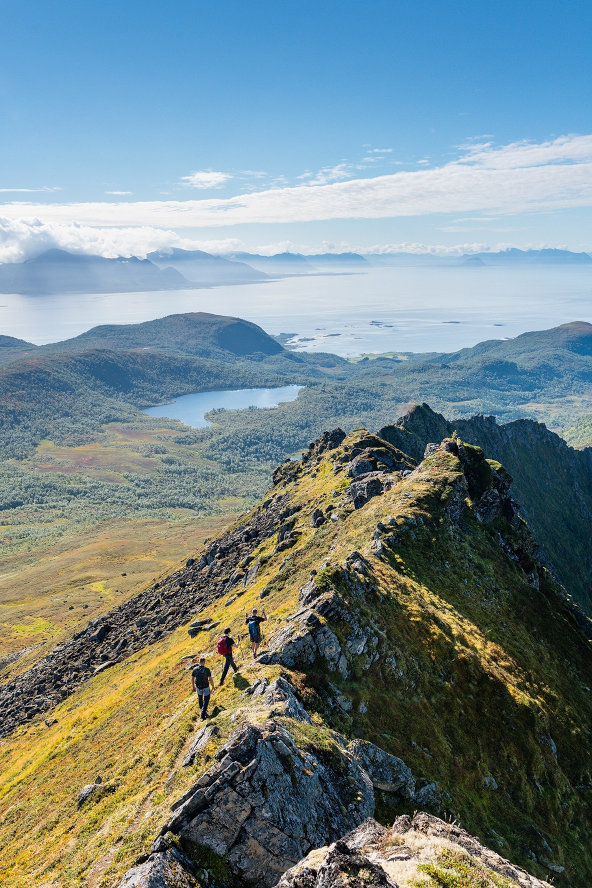 A group of hikers walking along the top of a hill with views over the landscape ahead.