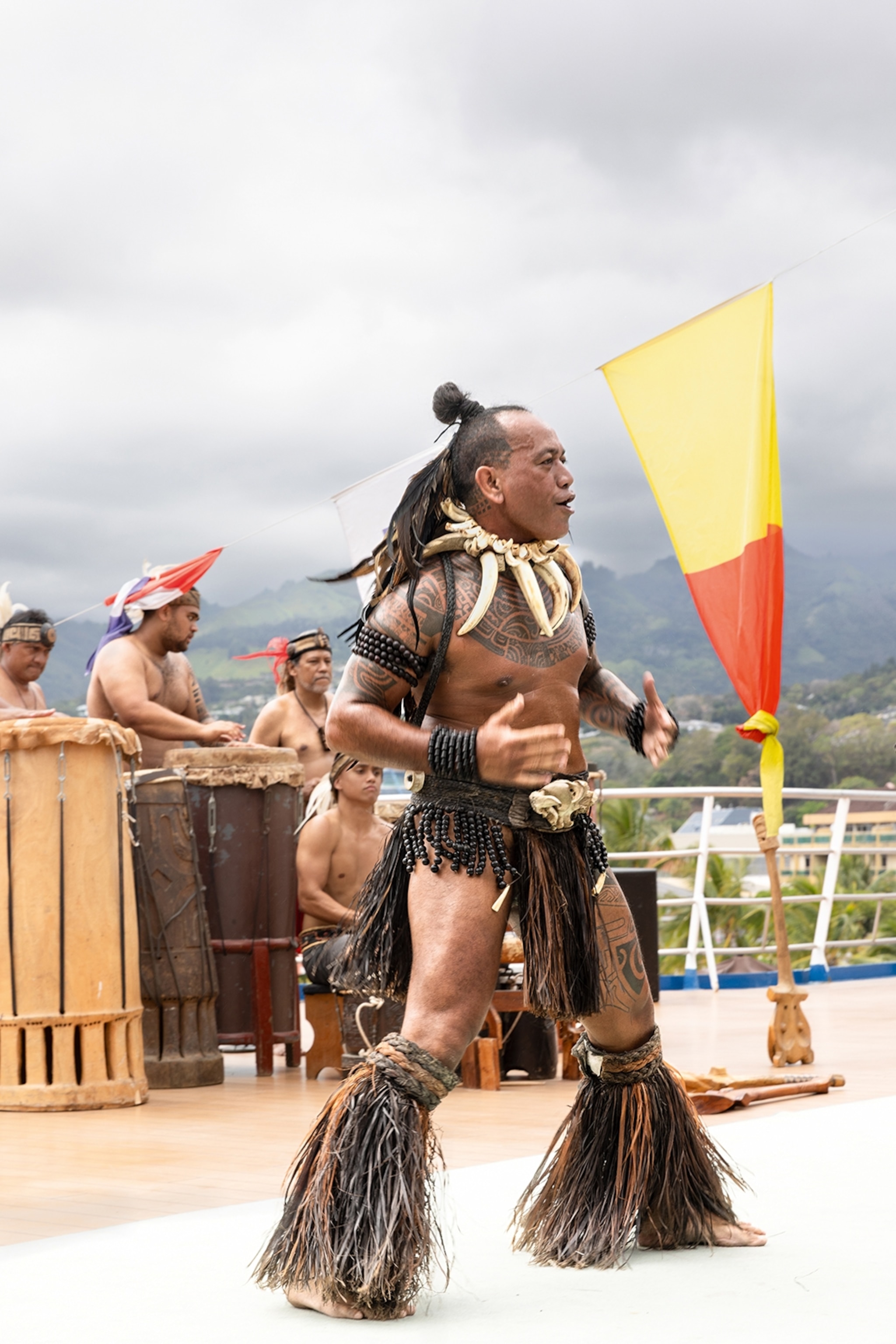 A local man with body tattoos, a teeth necklace and a beaded waist skirt, performing a traditional war dance on a cruise ship.