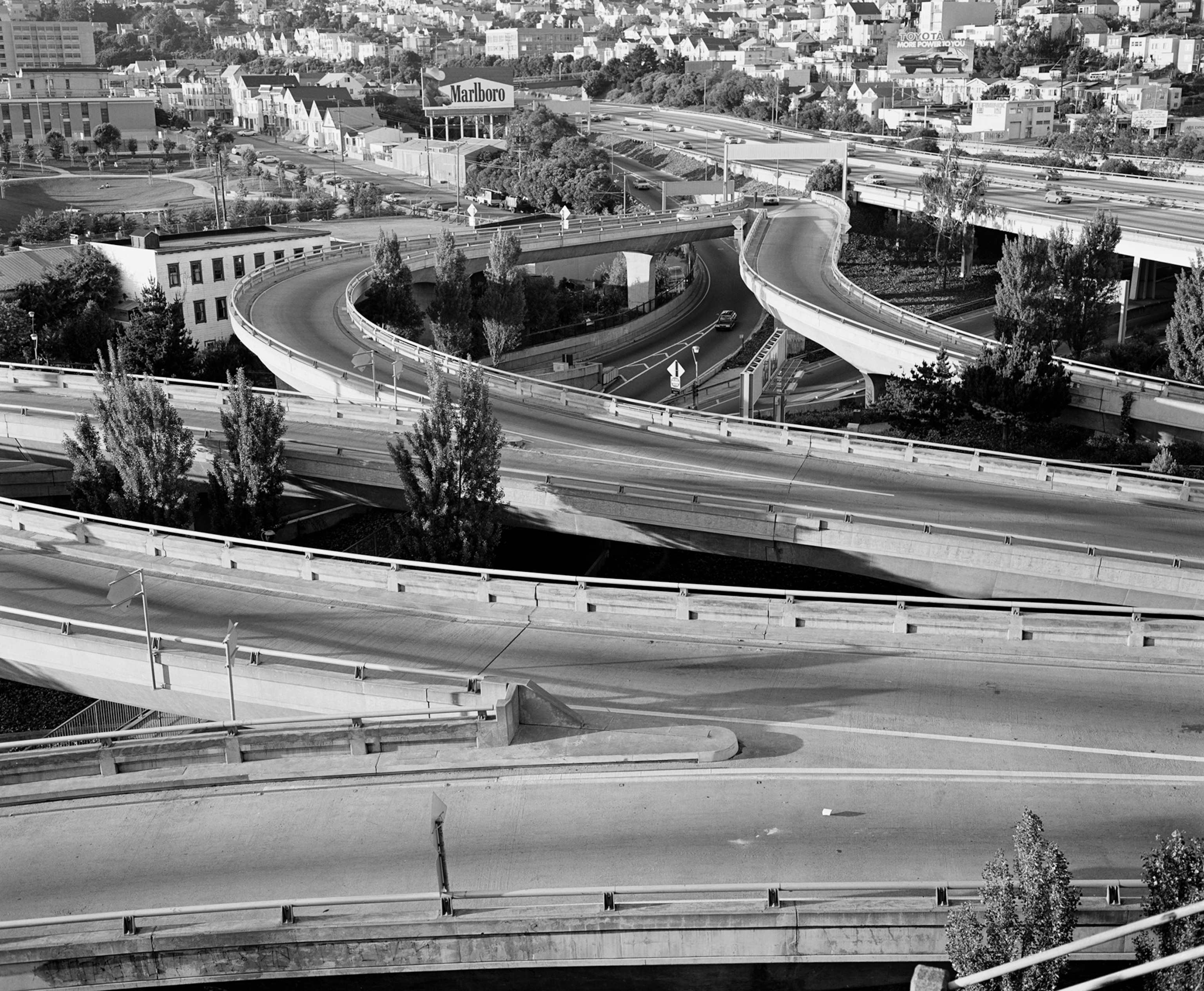 Black and white photo of a freeway, with houses in the distance.