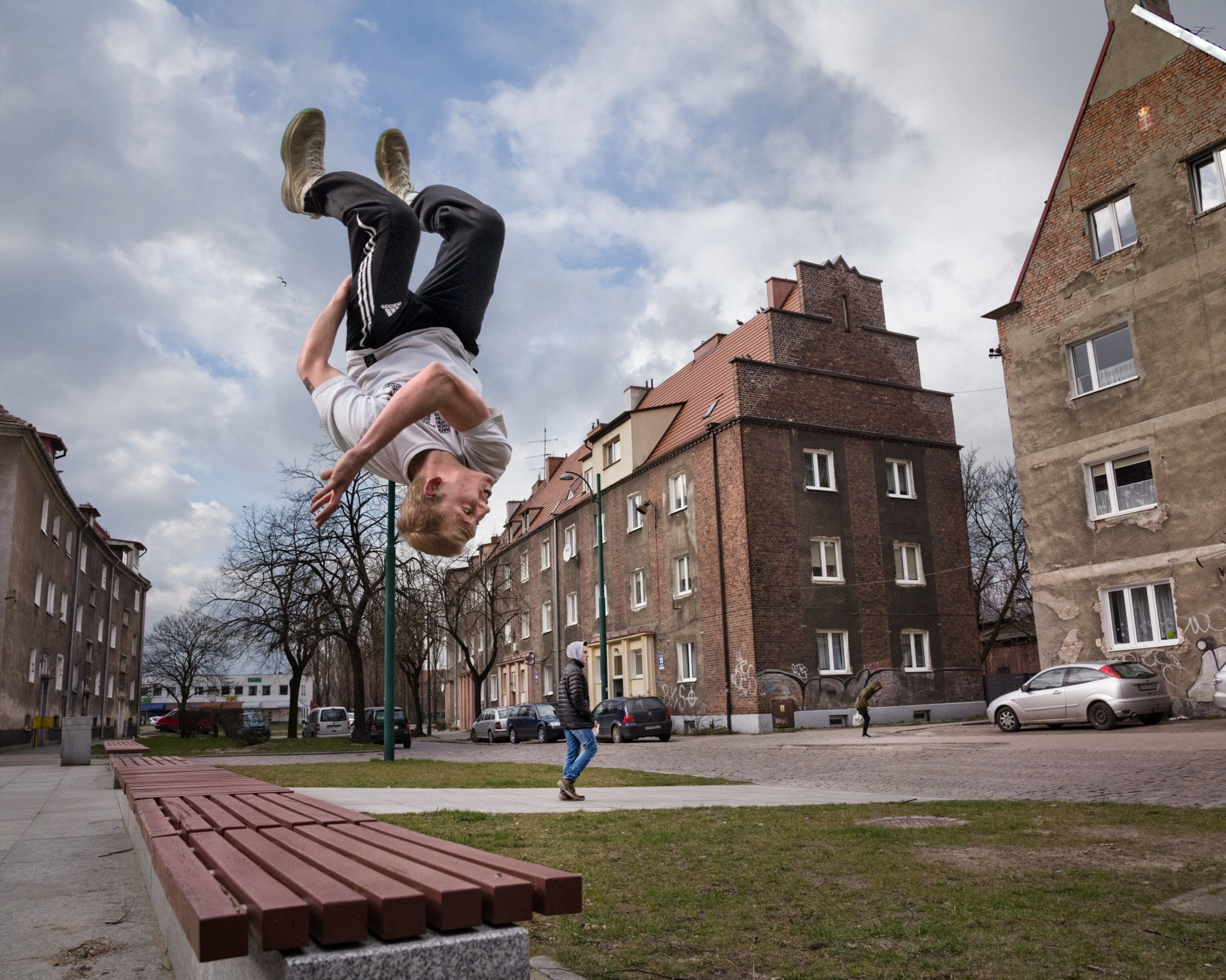 a boy backflipping along a bench on a sidewalk
