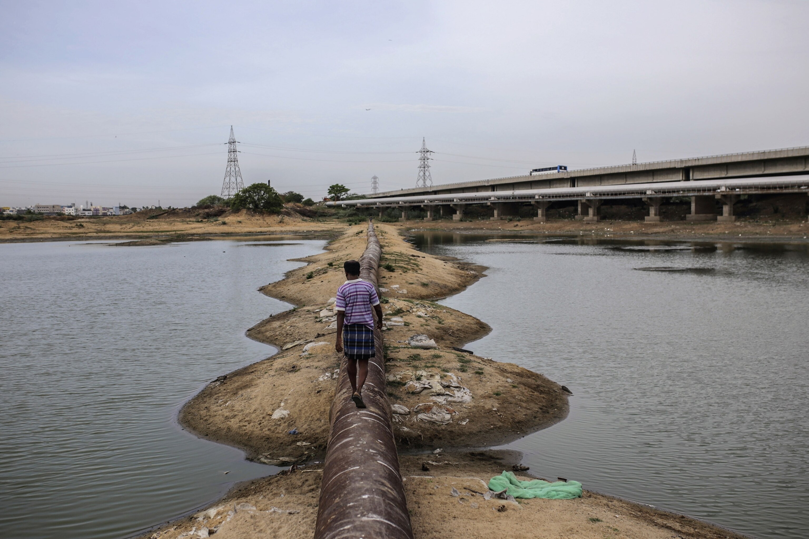 a man walking along a water pipe on the Porur Lake in Chennai, India.