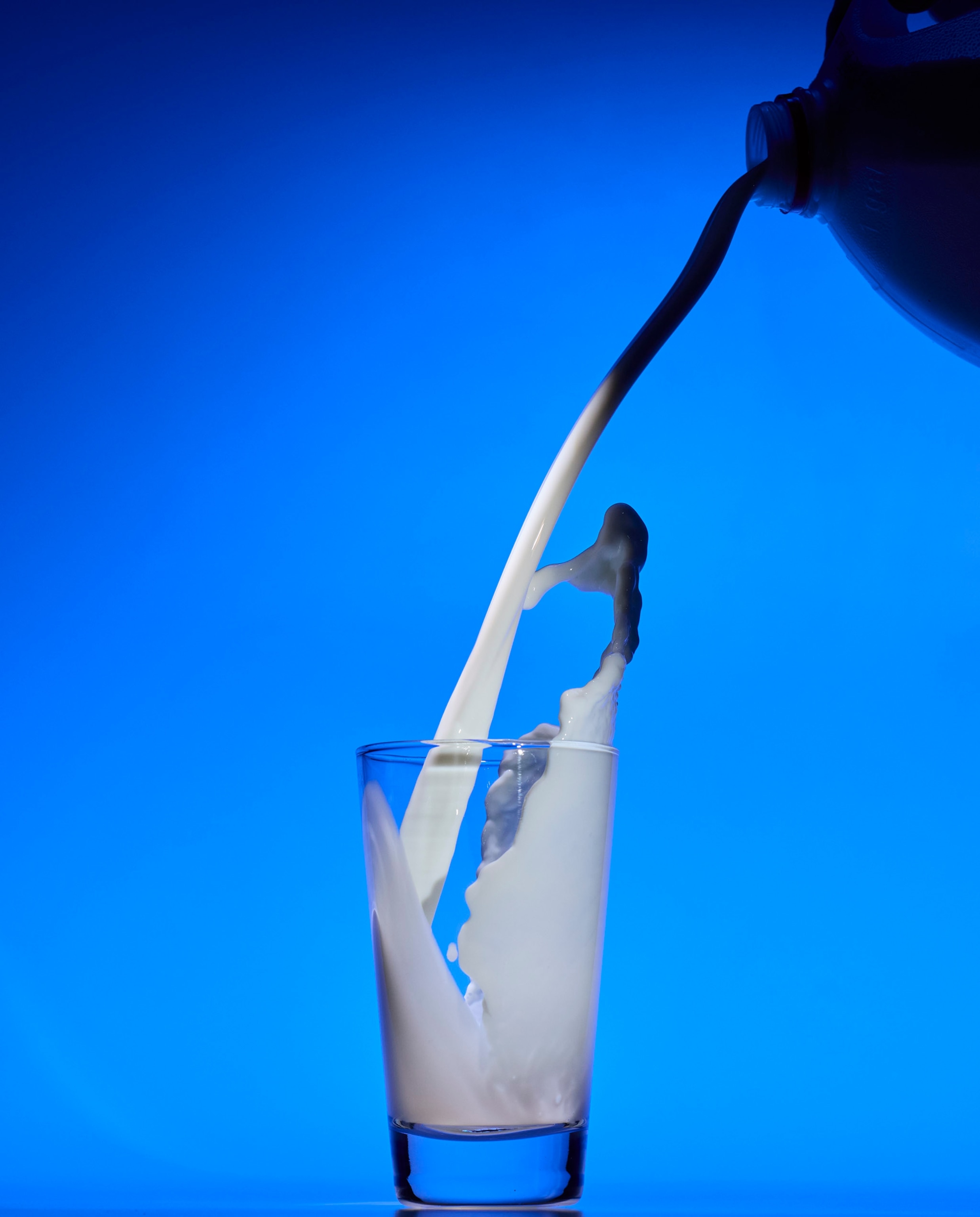 Milk pours into a tall glass against a blue background