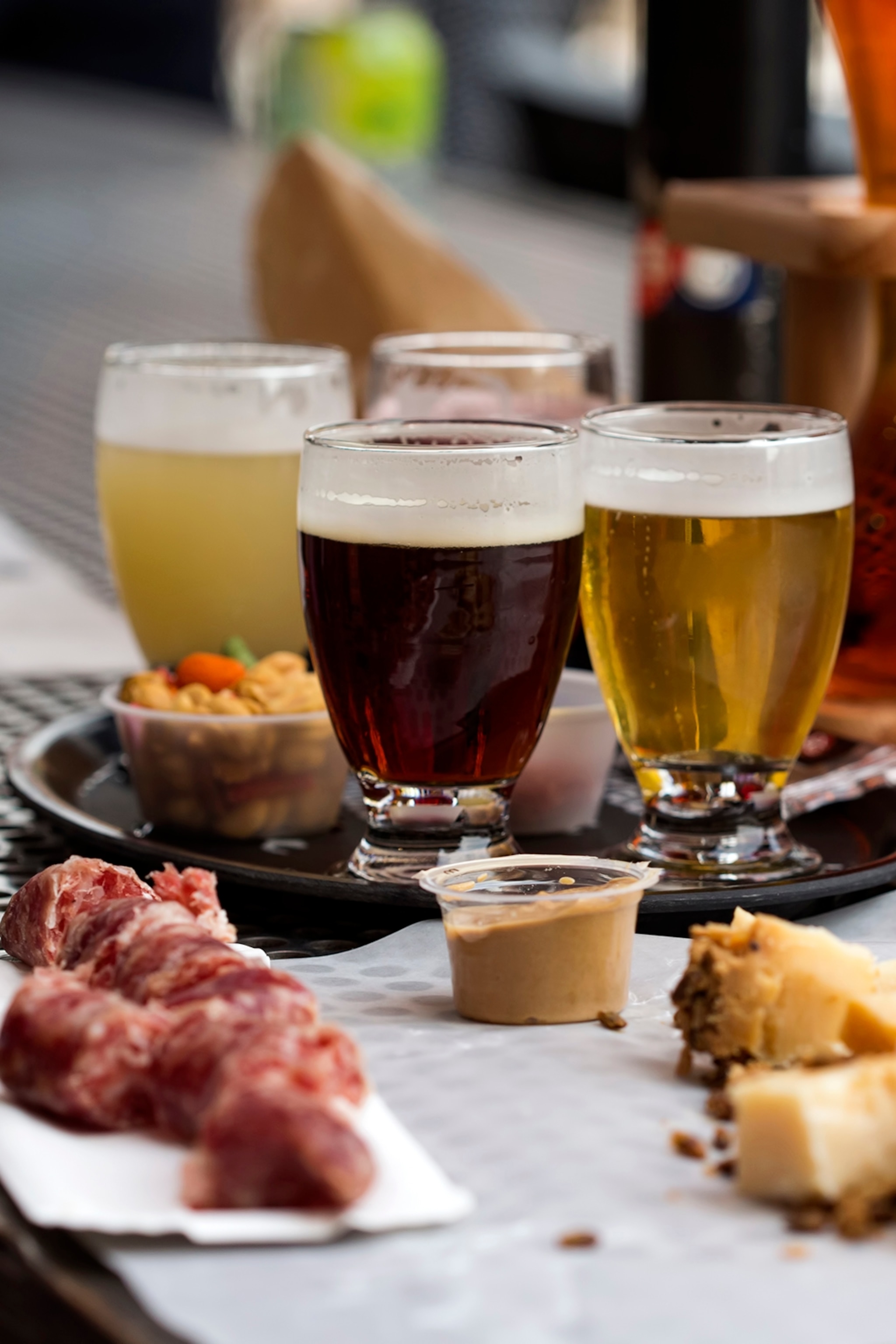A close-up on three glasses of beer with cured meats on a platter in front.