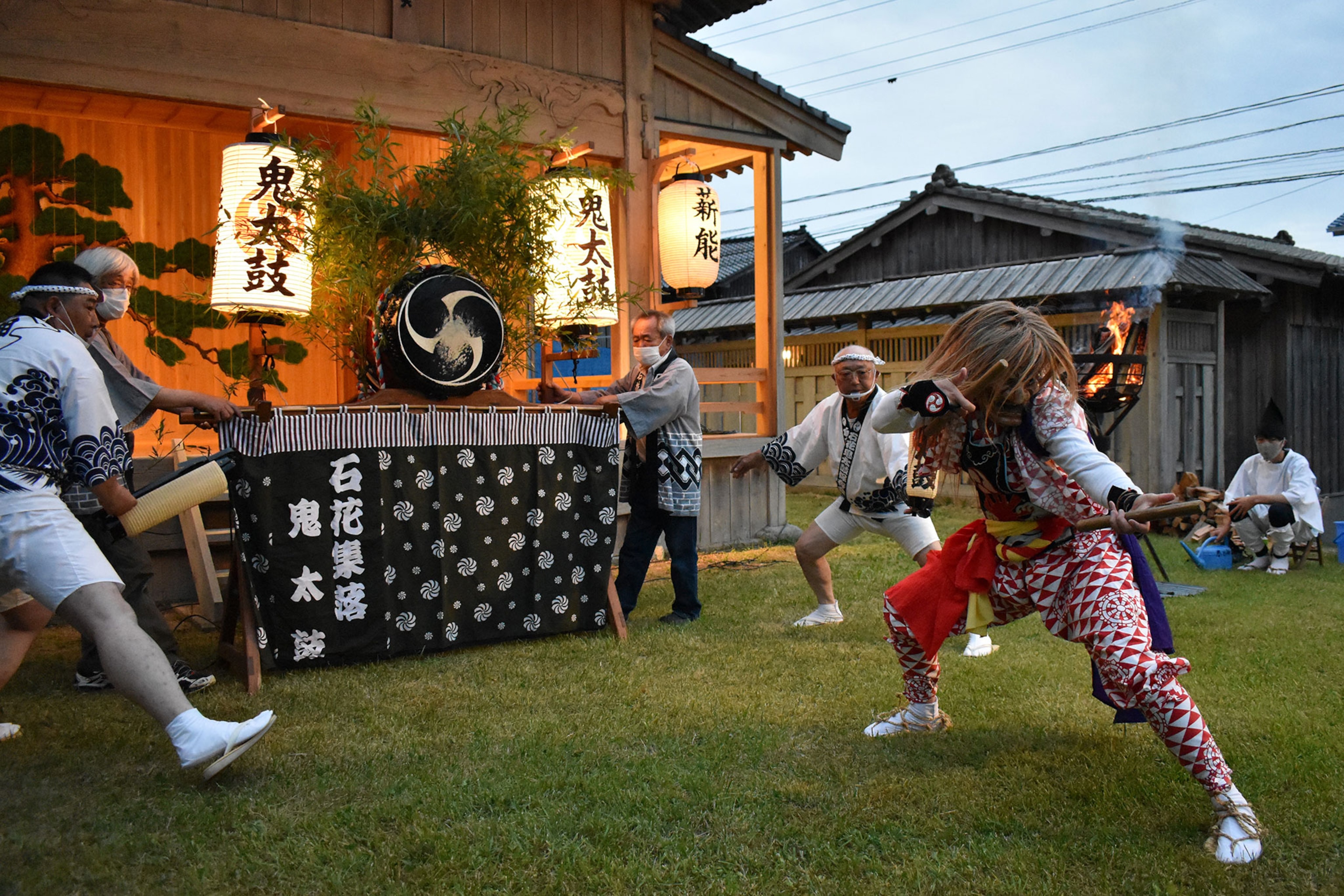 Performers dressed in traditional Japanese clothing surround a masked dancer.
