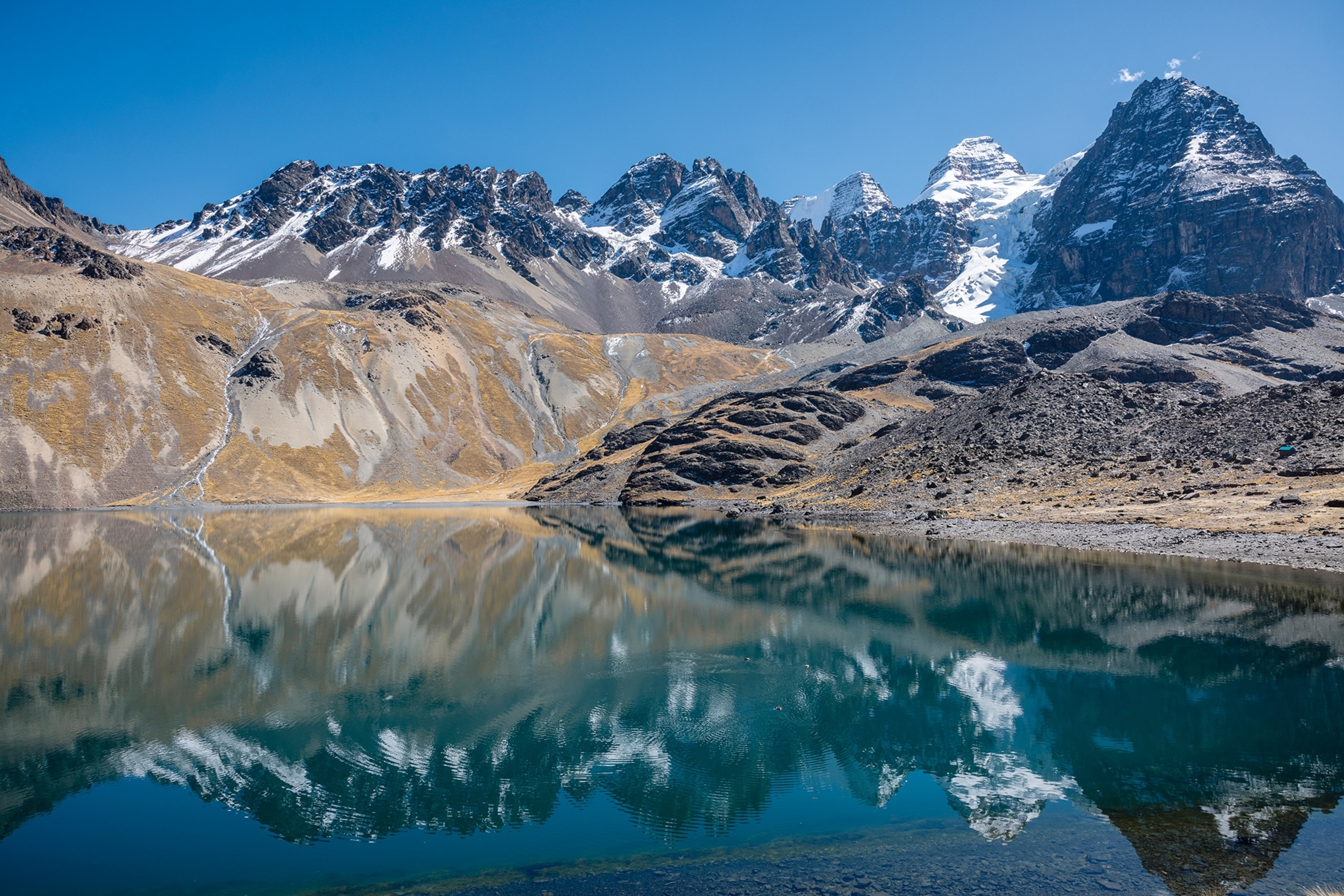 A clear, wide lake with a mountain ridge reflected on its surface.