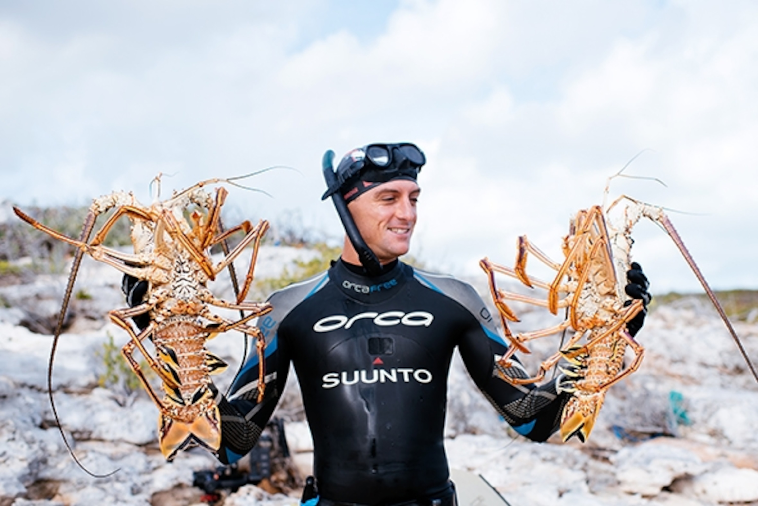 World champion free diver William Trubridge holds up the day's catch—two massive lobsters; Photograph by Max Lowe