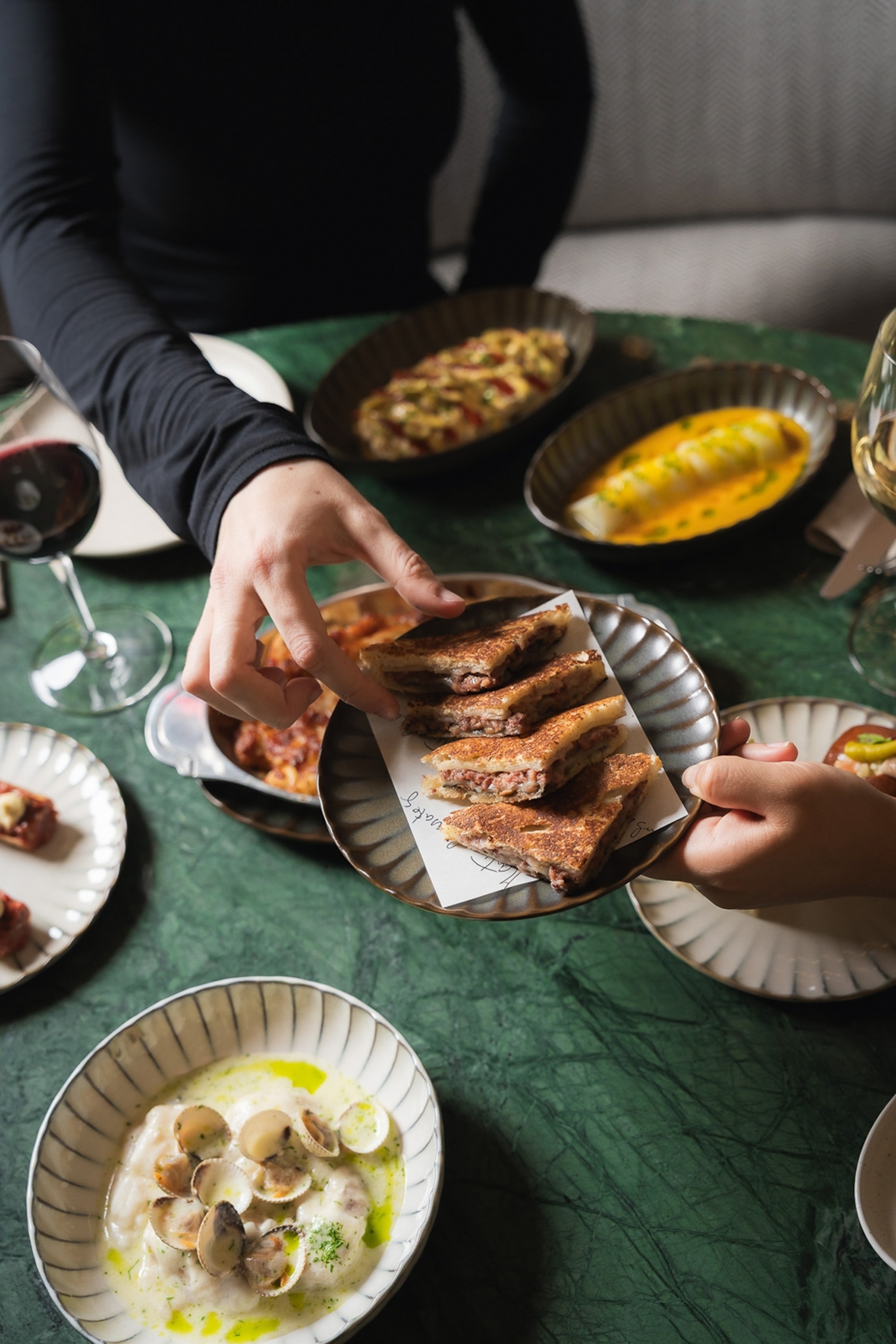 A hand offering a plate of toasties across a set table as another hand grabs one.