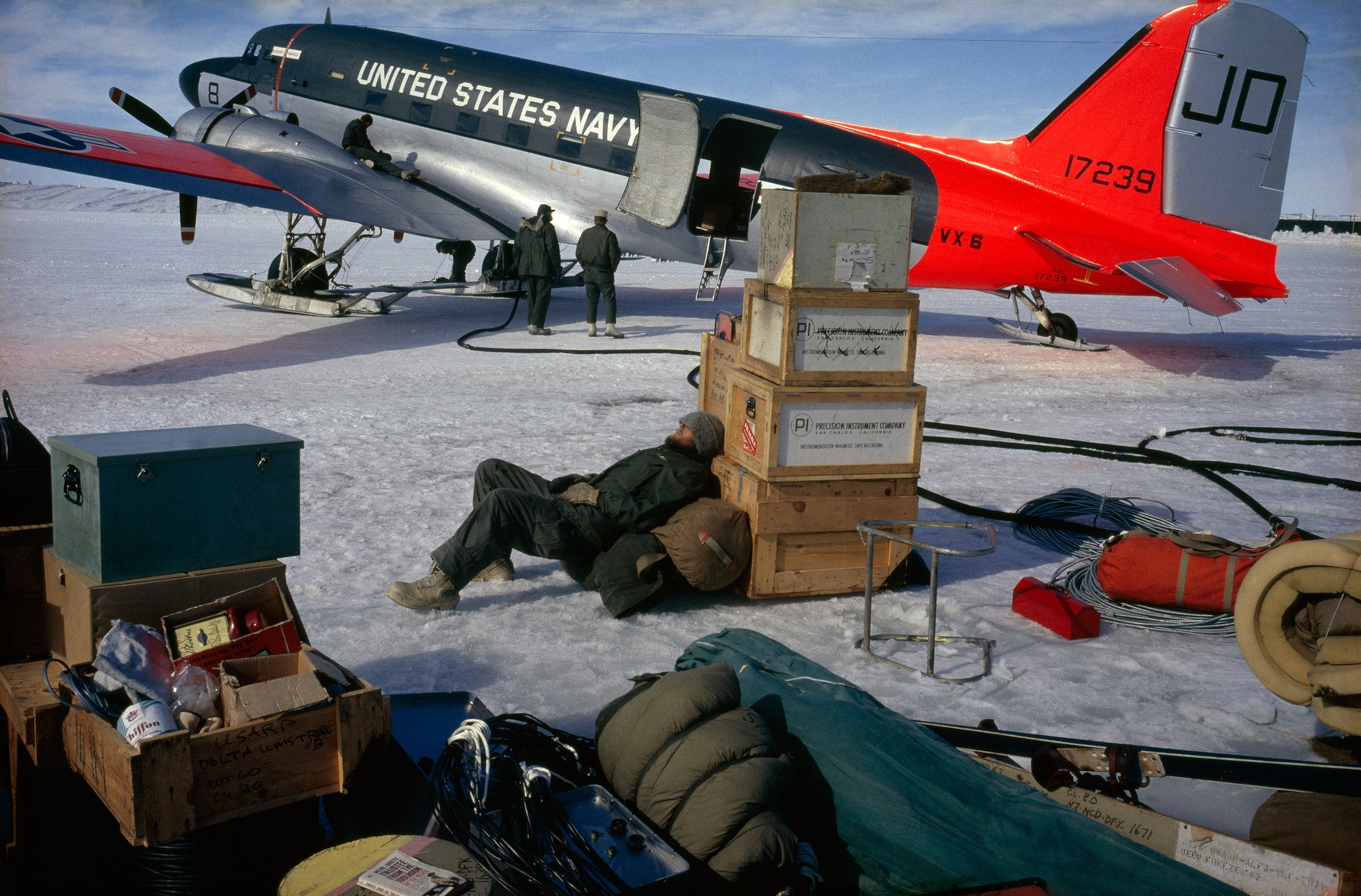 man sleeping against boxes with plane in background