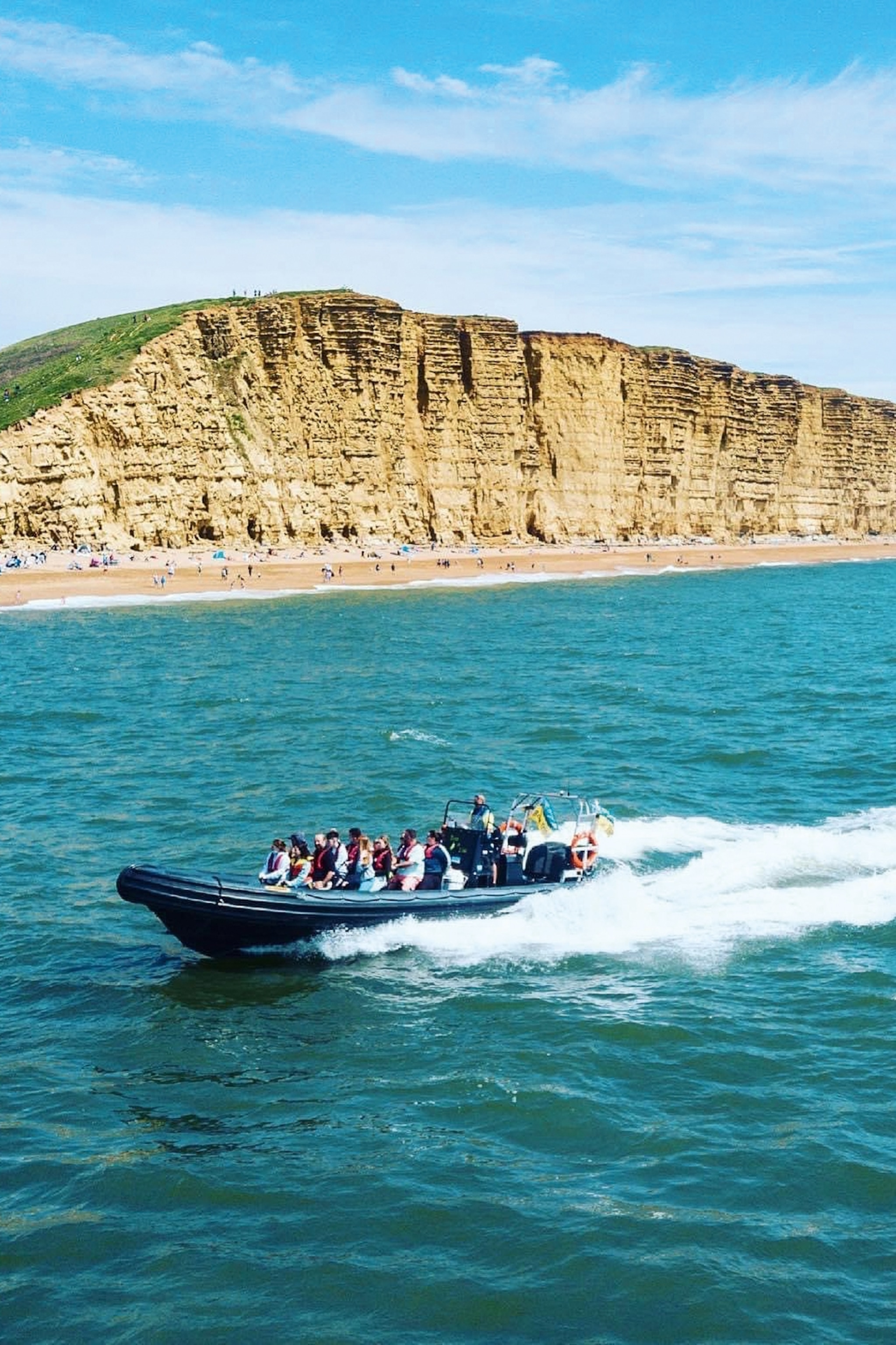 A speeding boat with a group of spectators going a long a coast line.