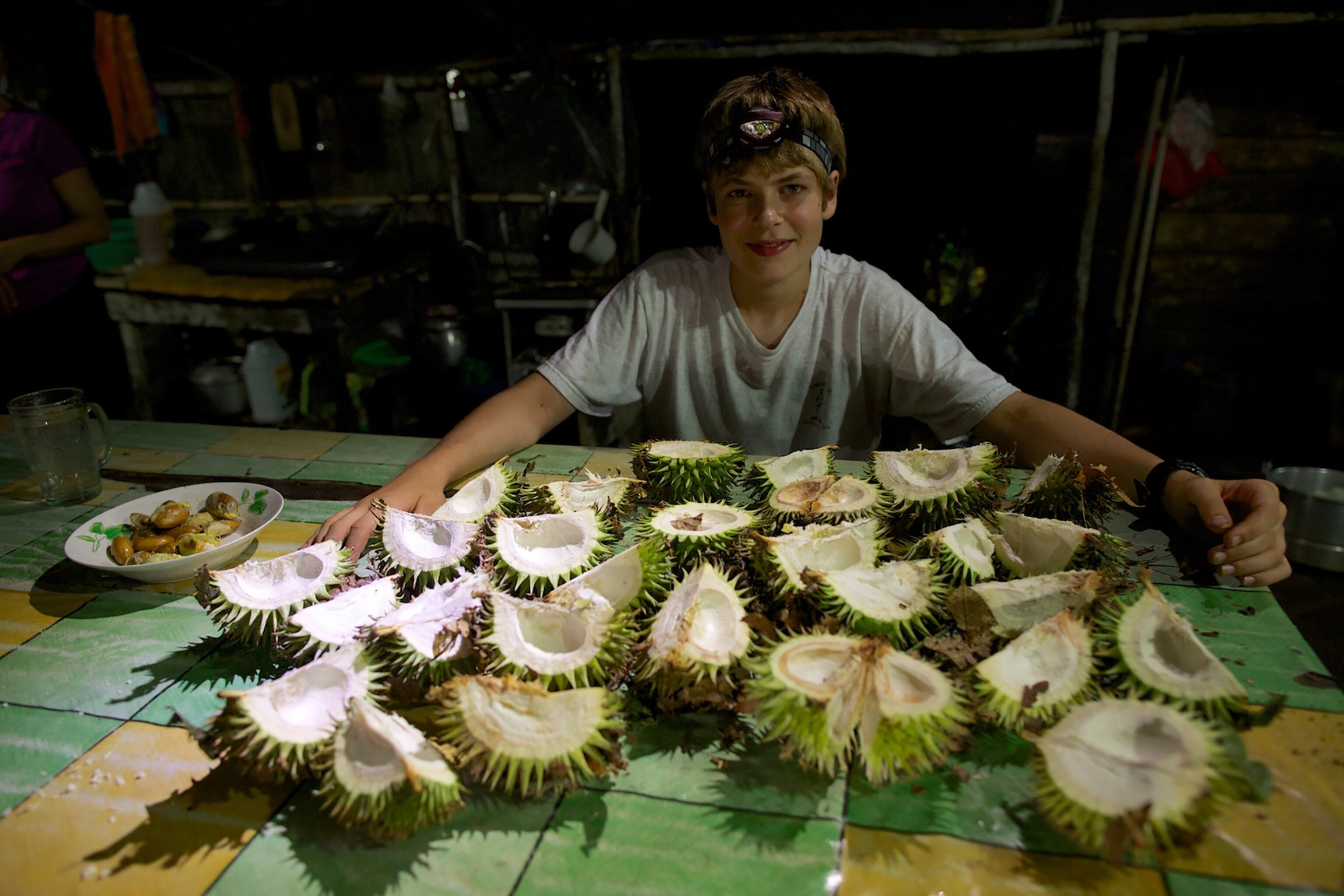 Russell Laman sitting at a table full of opened durians in the research camp