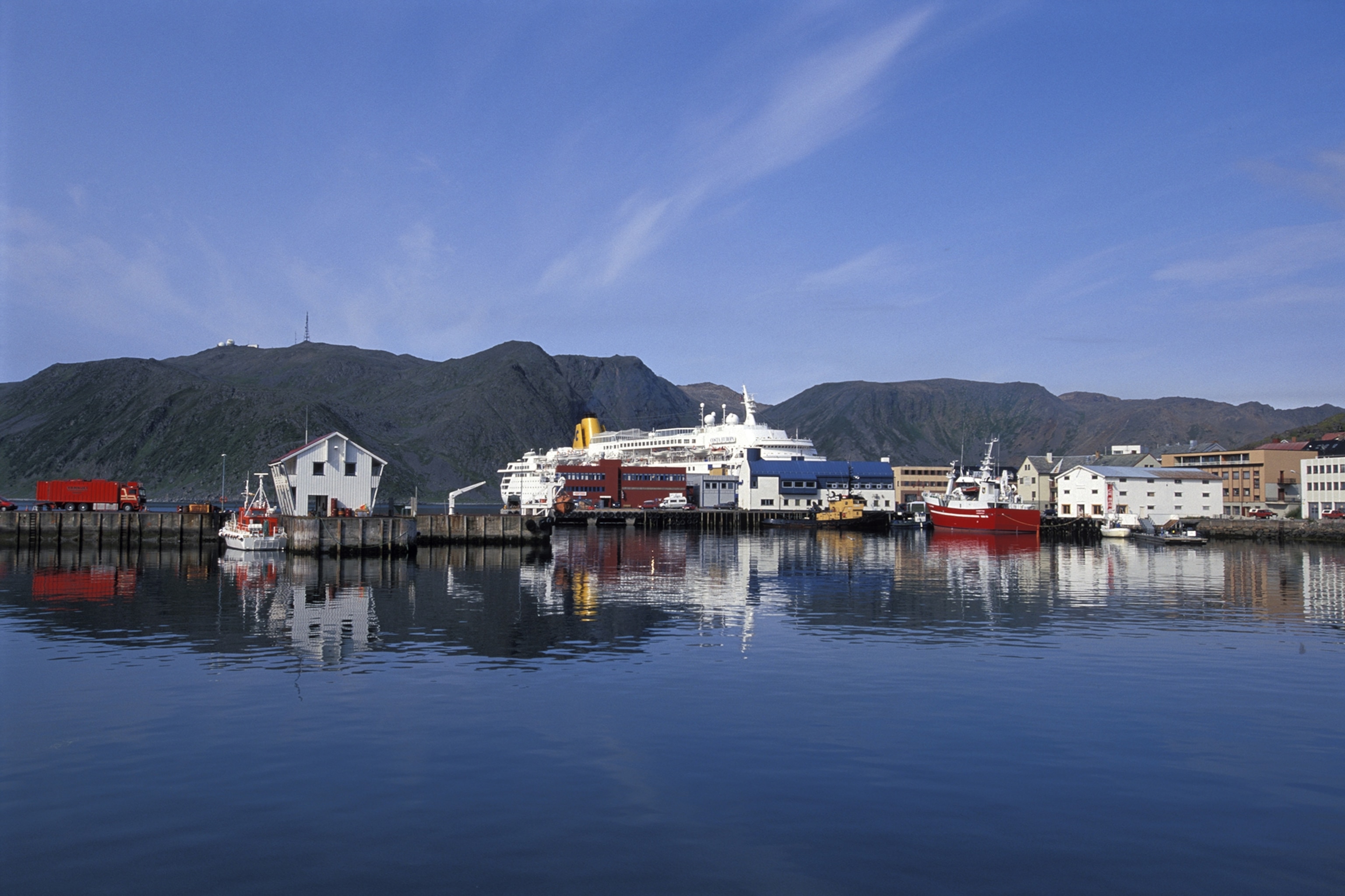 Fishing boats and small buildings are seen in the harbour of Gjesvær on a bright summer day.