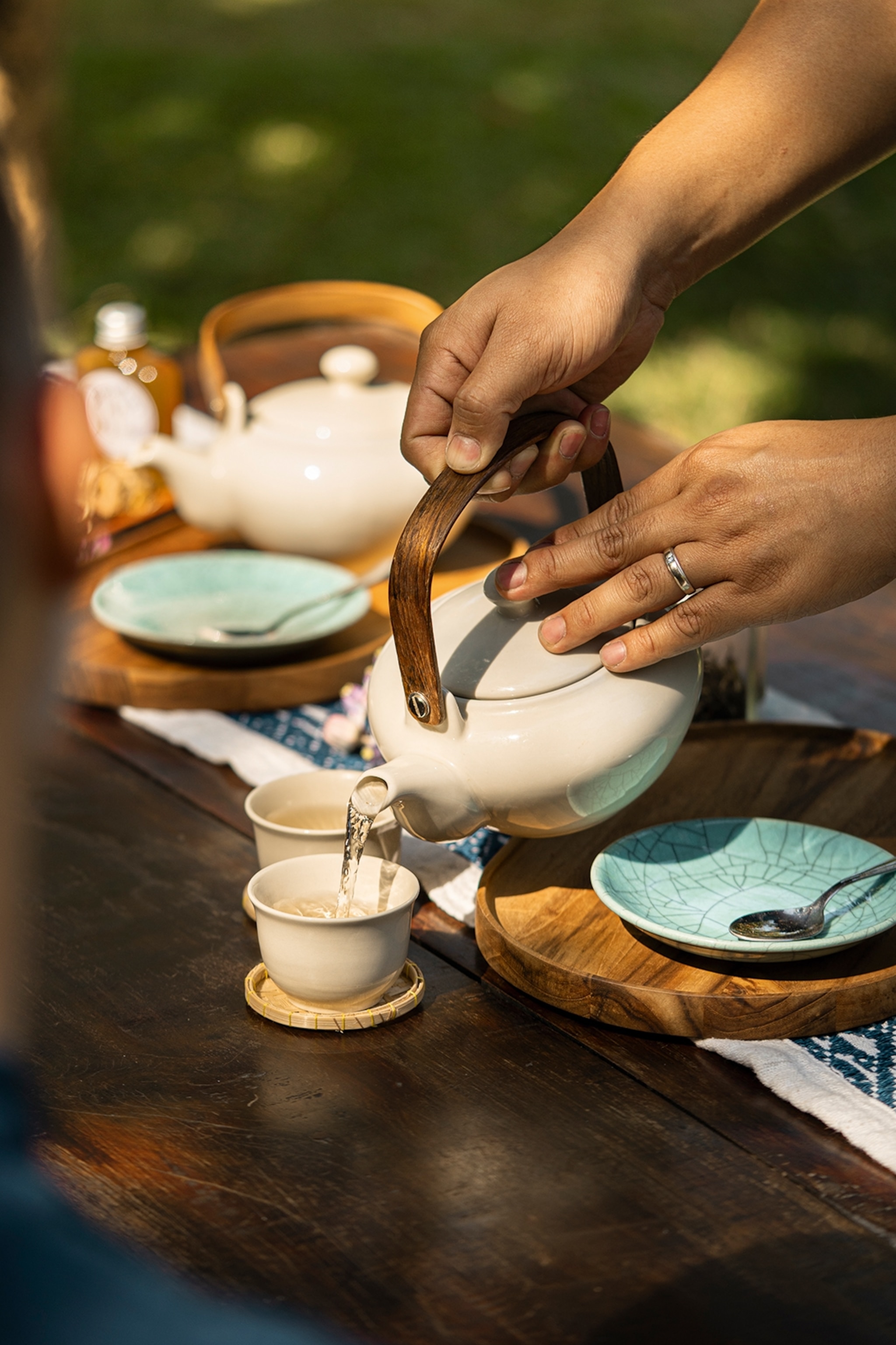 A pair of hands serving tea in a fancy tea set outdoors.