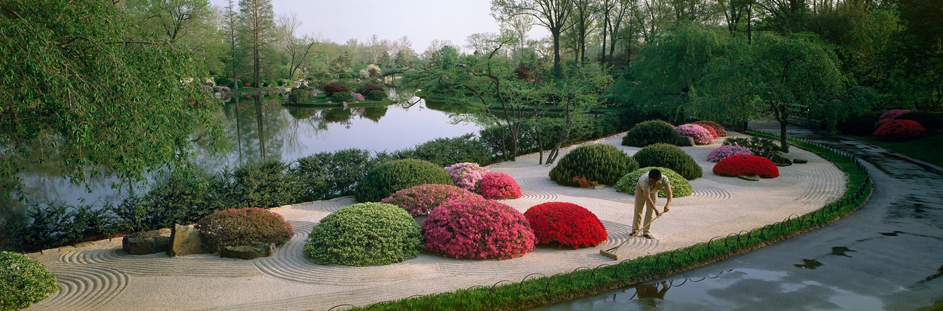 A gardener rakes gravel into ripples at a Japanese garden.