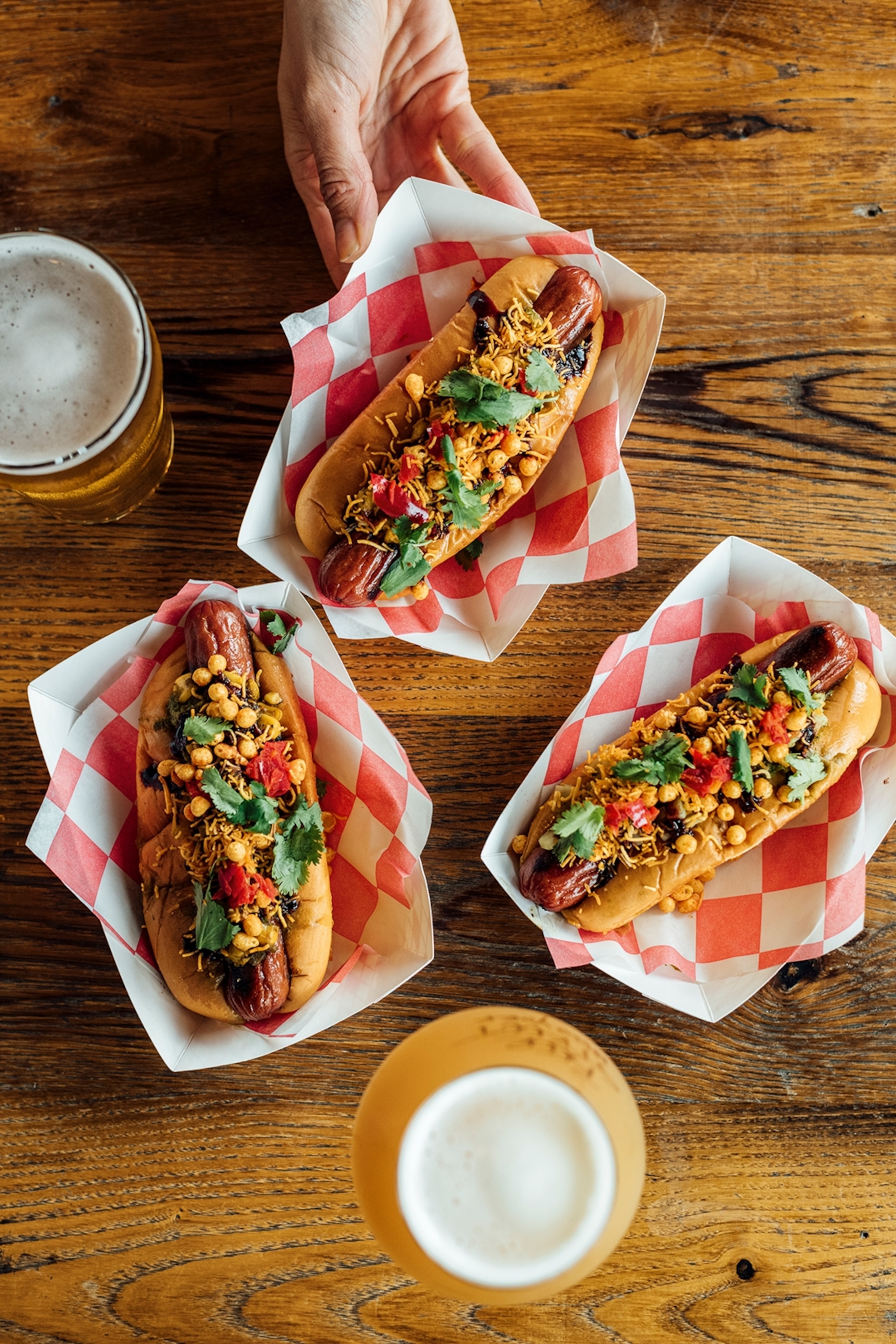Three hot dogs in individual paper boats, topped with spiced chaat.