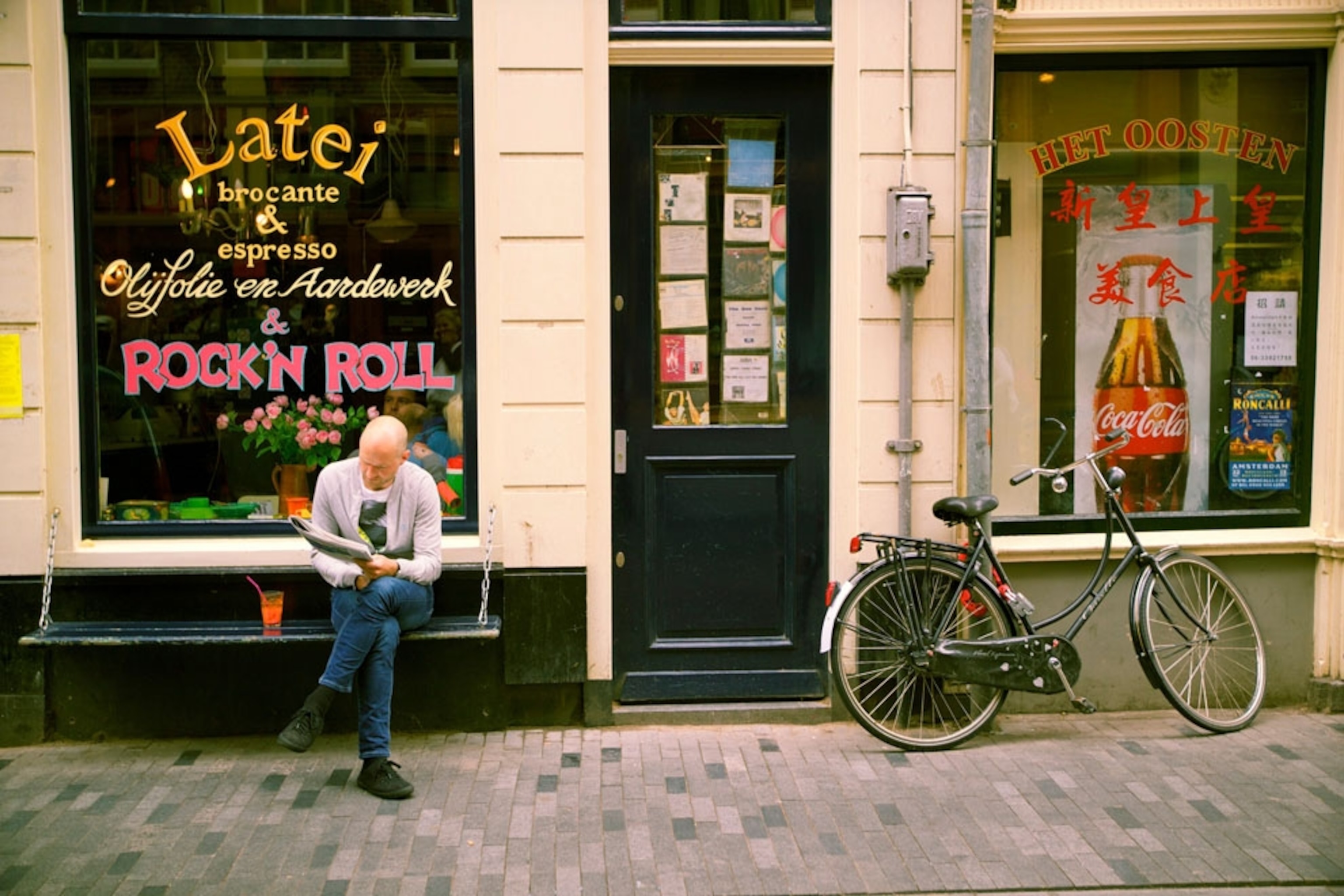 A man reading a paper on a bench outside of a cafe in Amsterdam