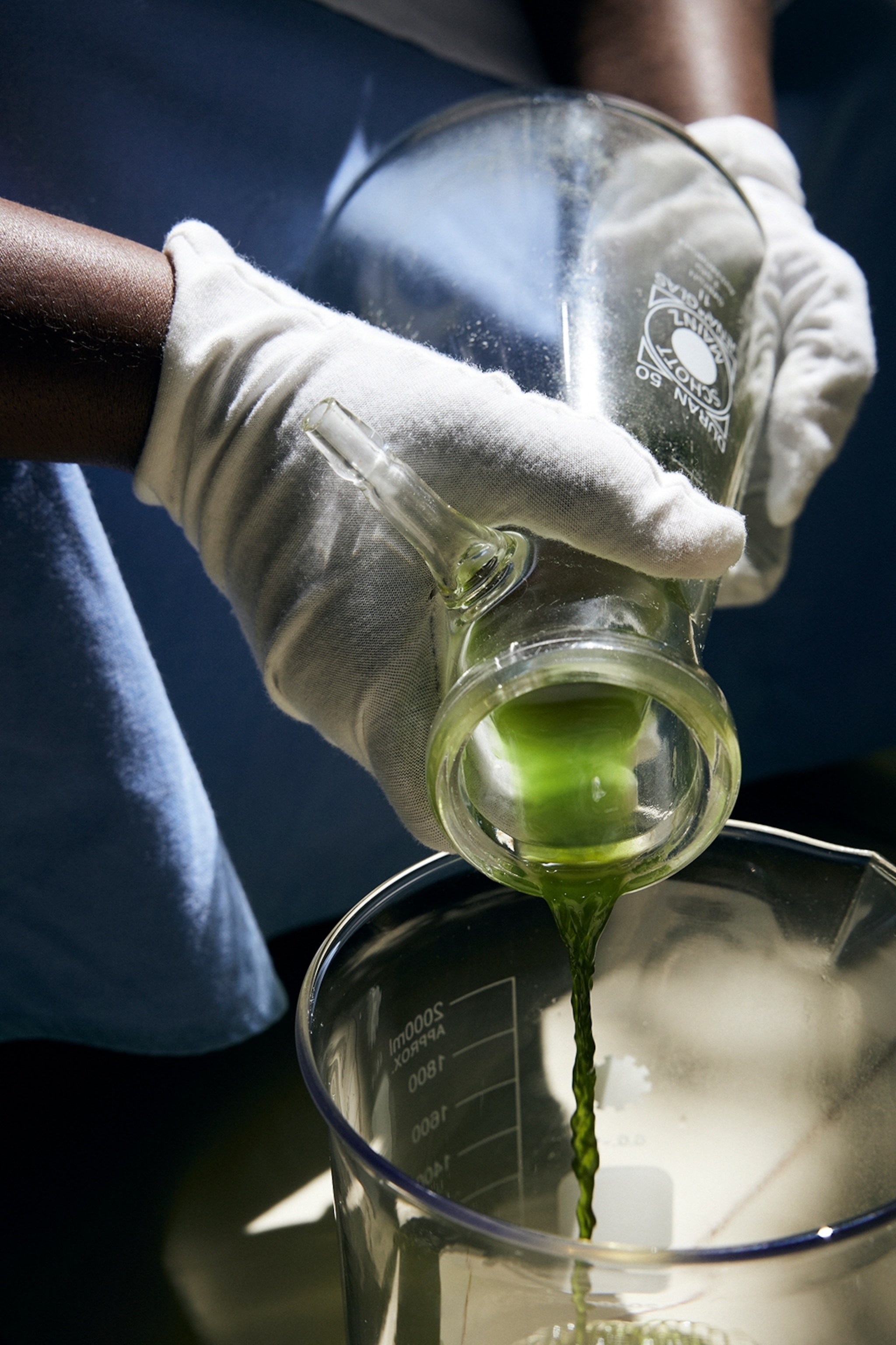A concentrated, green oil is poured into a measurement container in a lab setting.