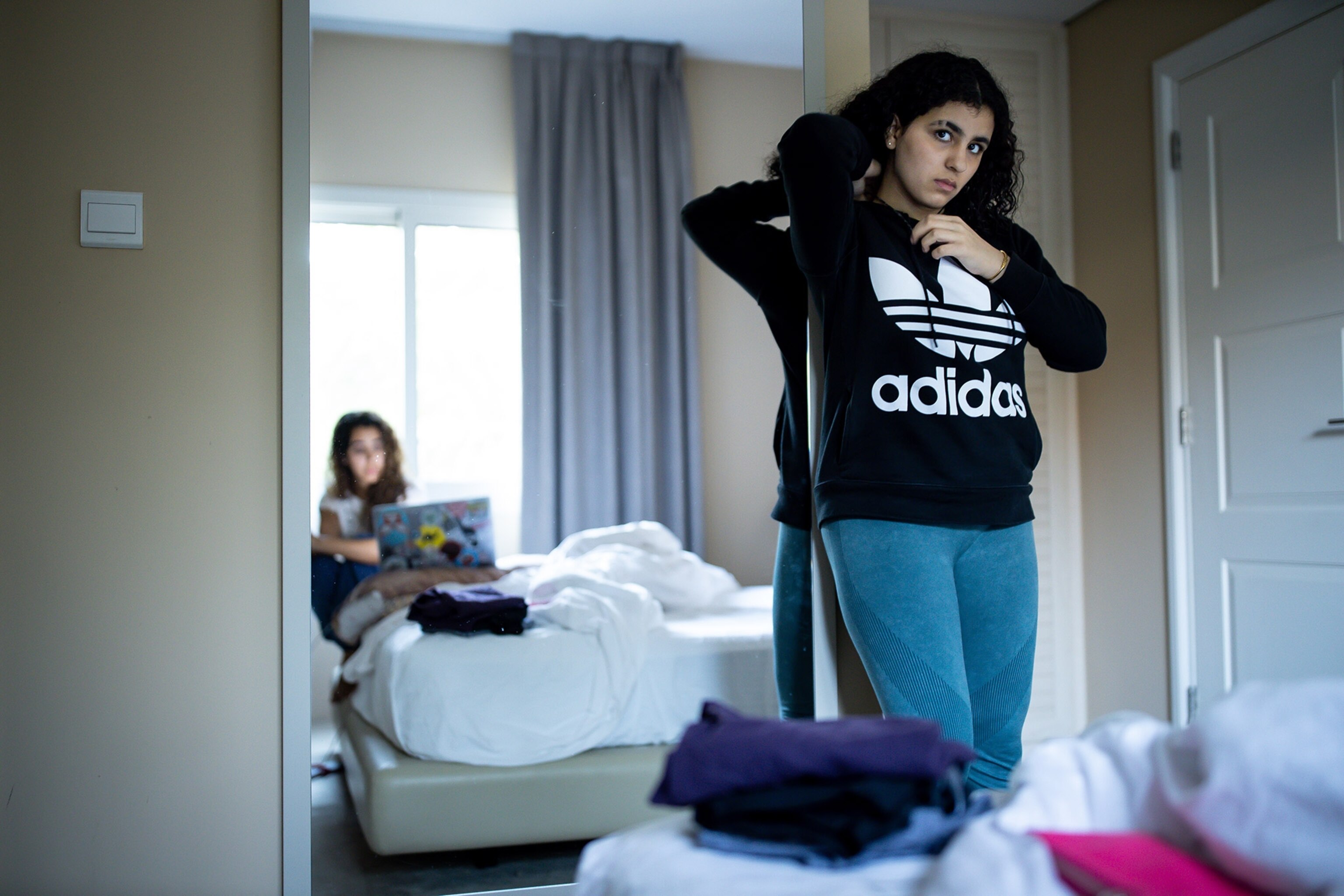 a daughter adjusting her sweatshirt with her mother reflected in the mirror