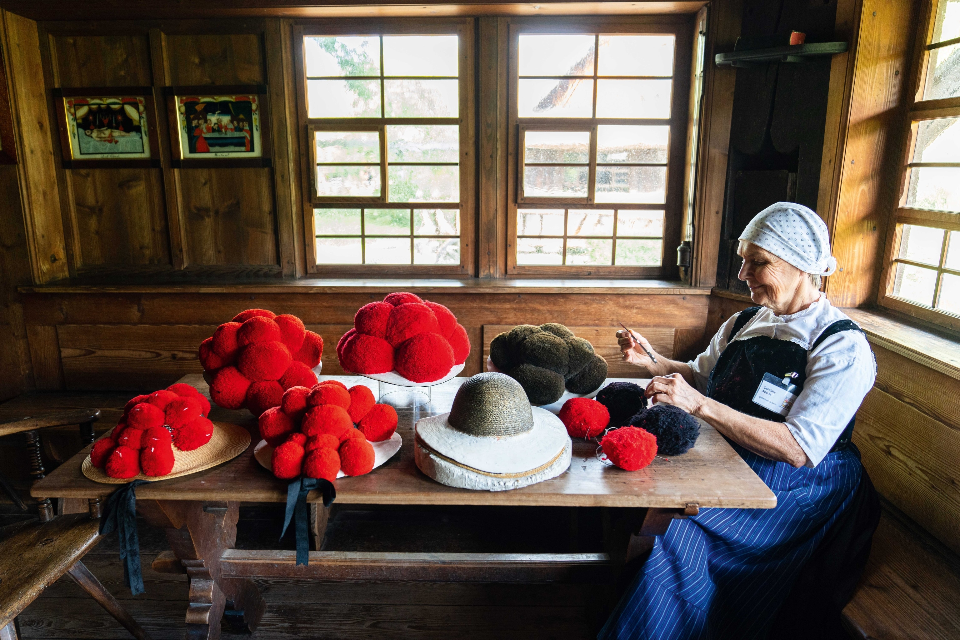 An old woman knits at a table full of balls of red wool.