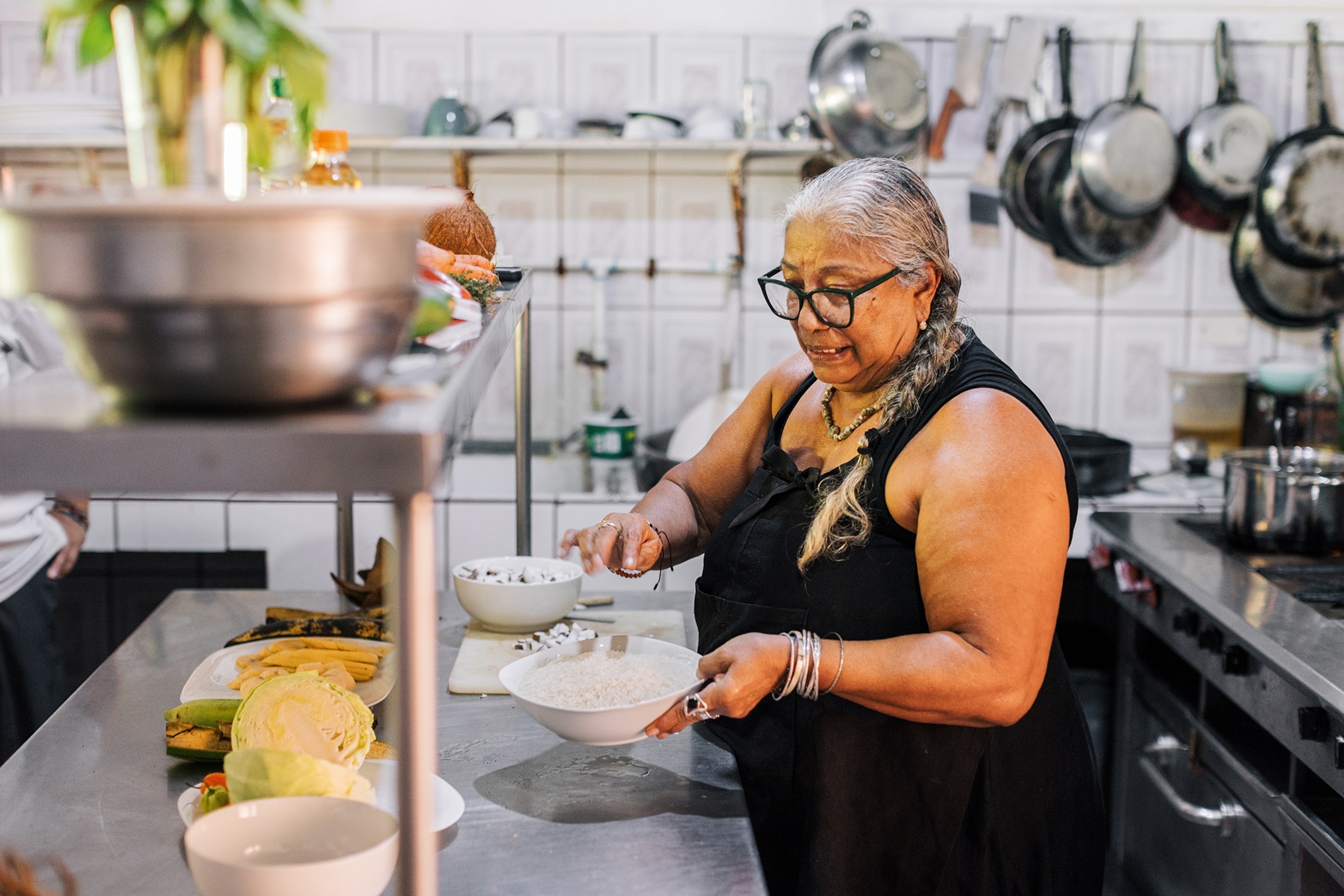 A Caribbean woman plating a rice dish in an industrial kitchen.