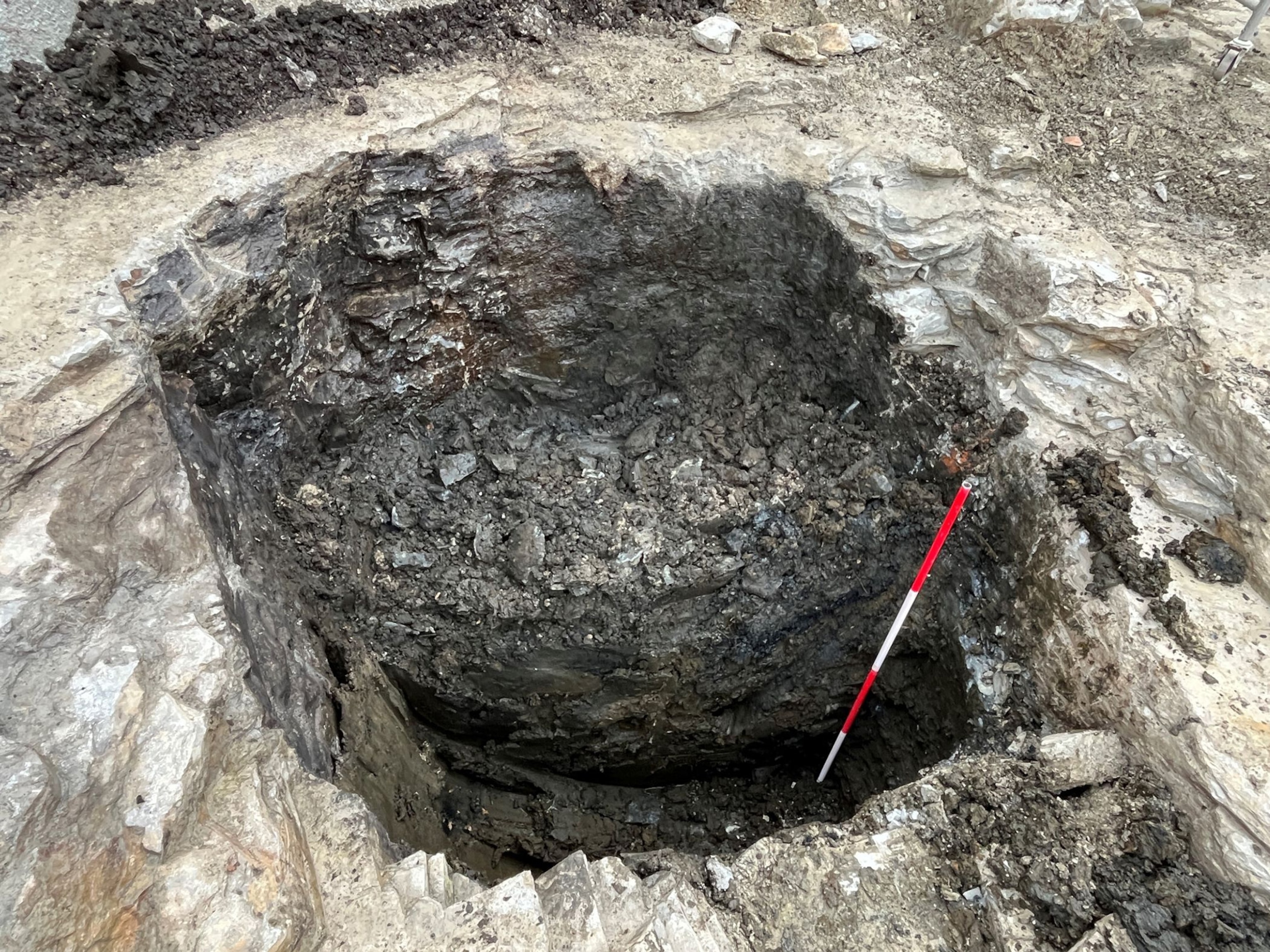A large pit dug out a stone and gravel with a red and white measuring stick placed at the bottom.