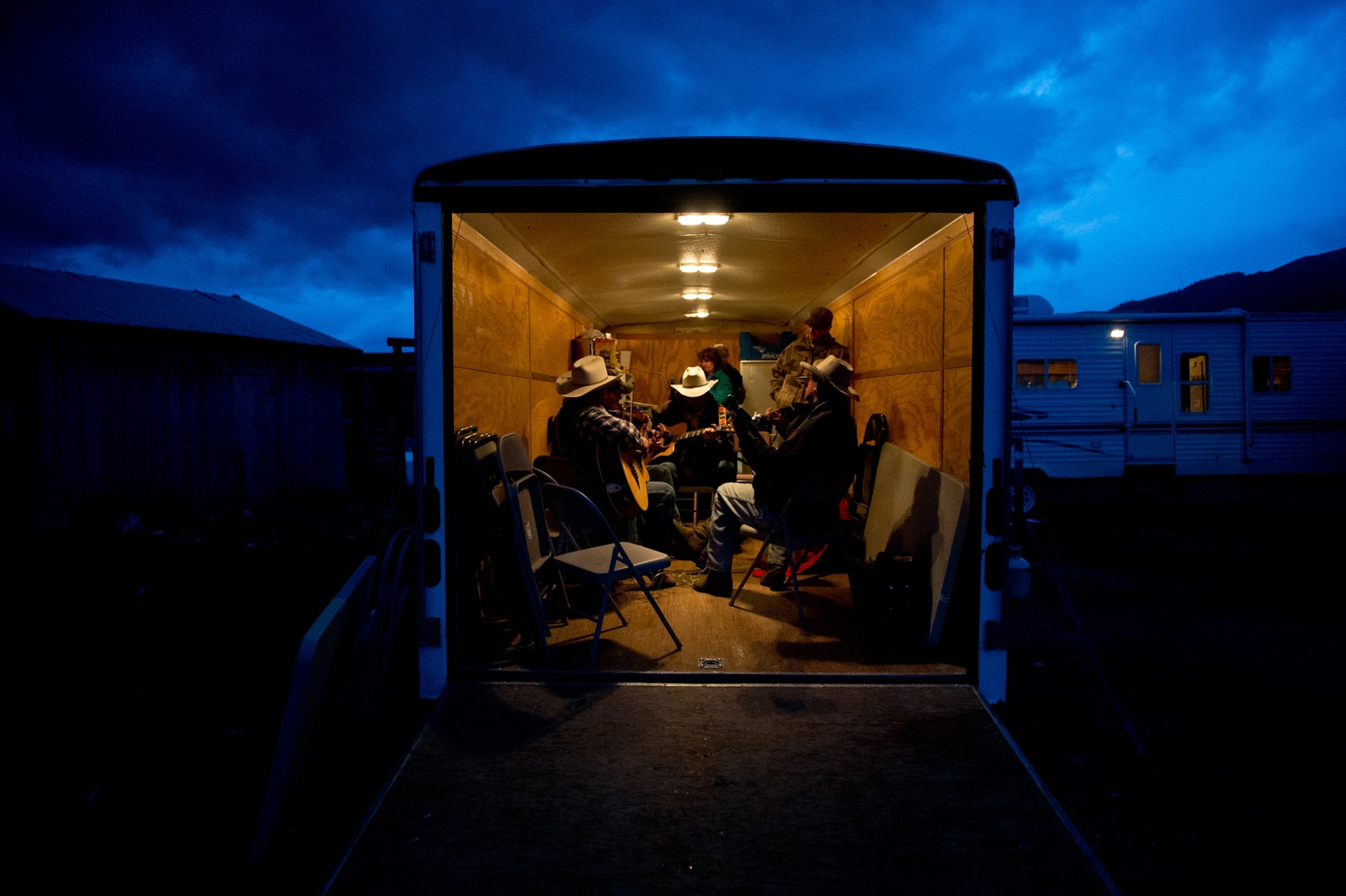 Ranchers gathered in a trailer as some sit and play instruments.