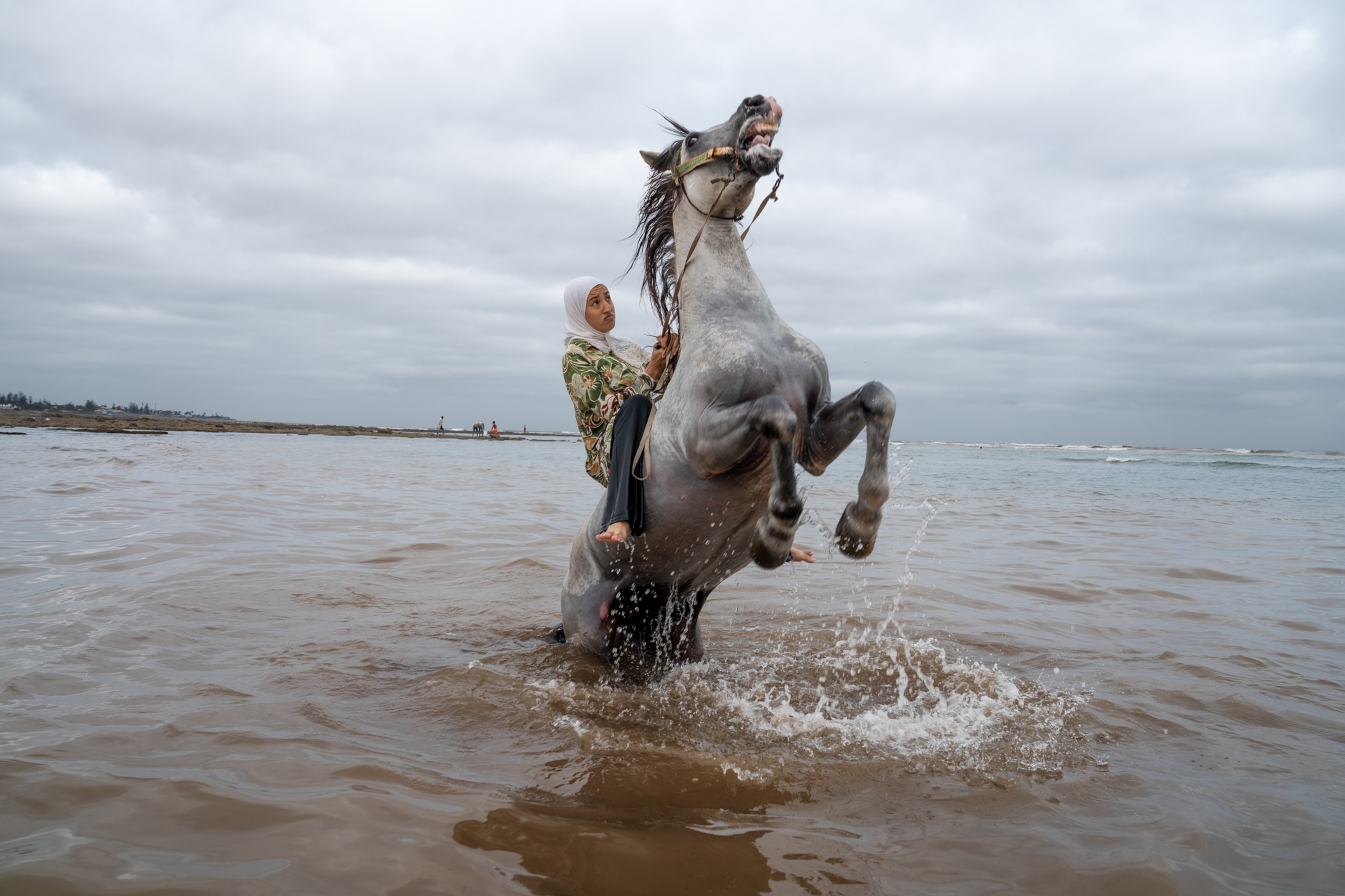 A woman sits on her horse in the water as the horse stands on its hind legs.