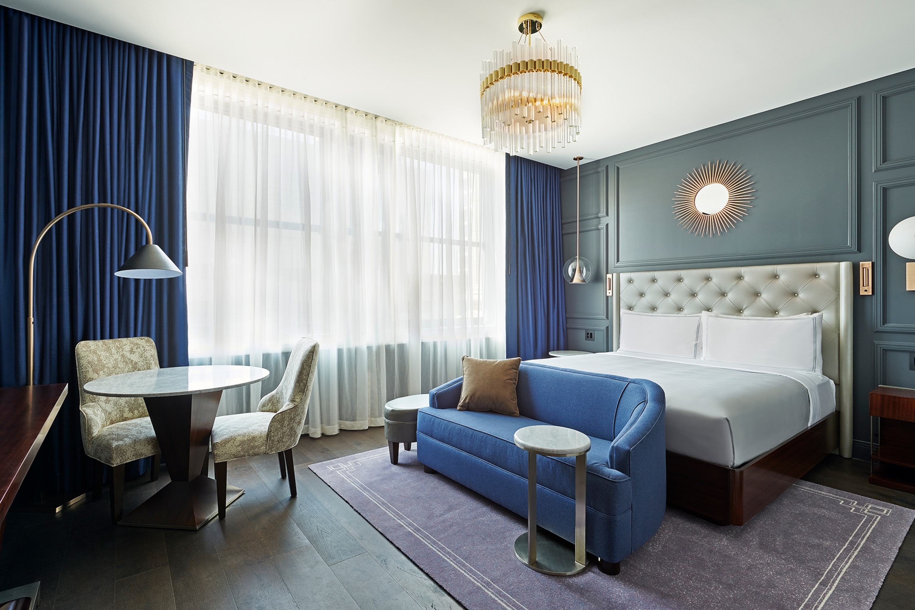 A hotel room with purple curtains, carpet and sofa.