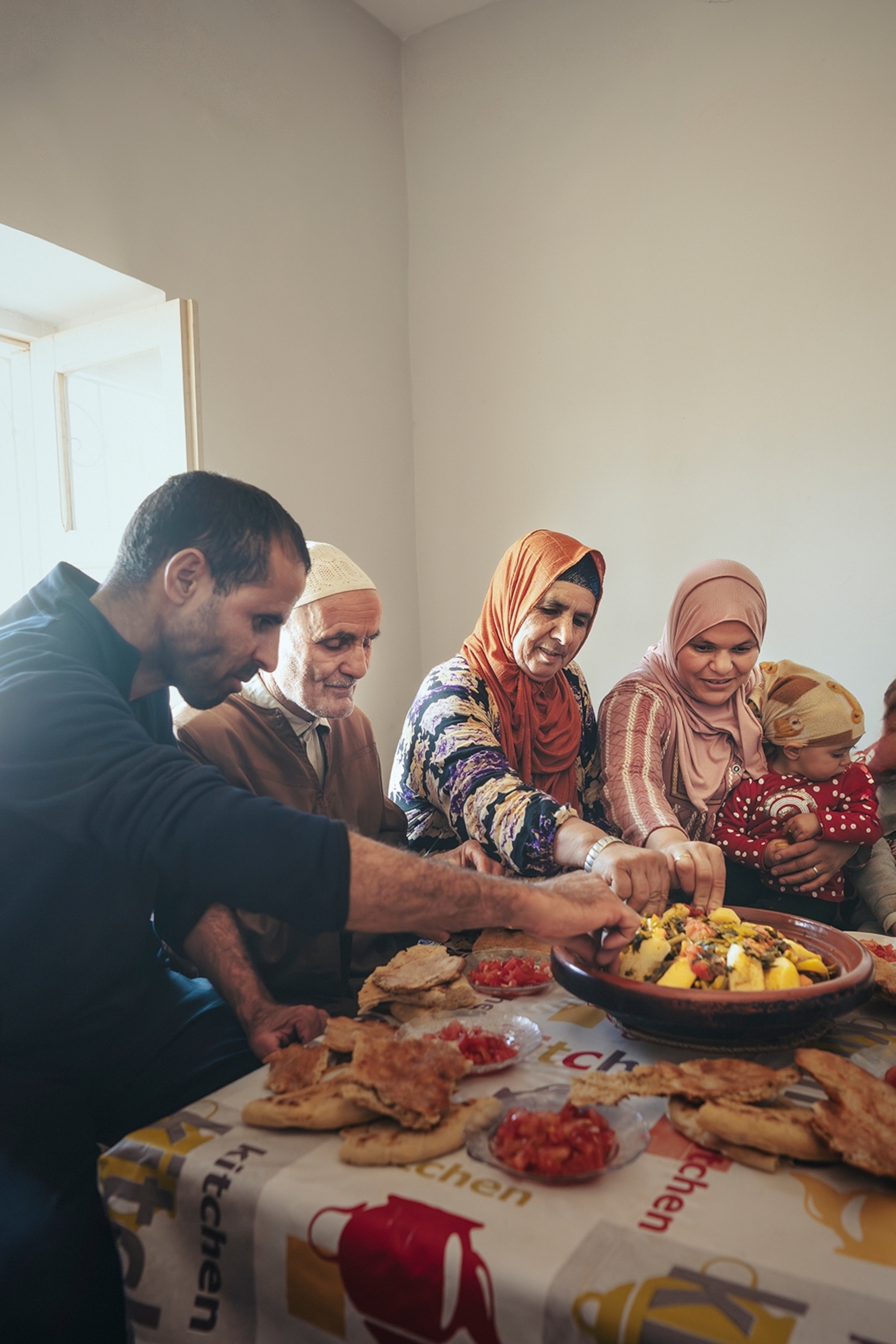 A small family sat around a set dining table, all reaching with their hands into the goat tagine at the center.